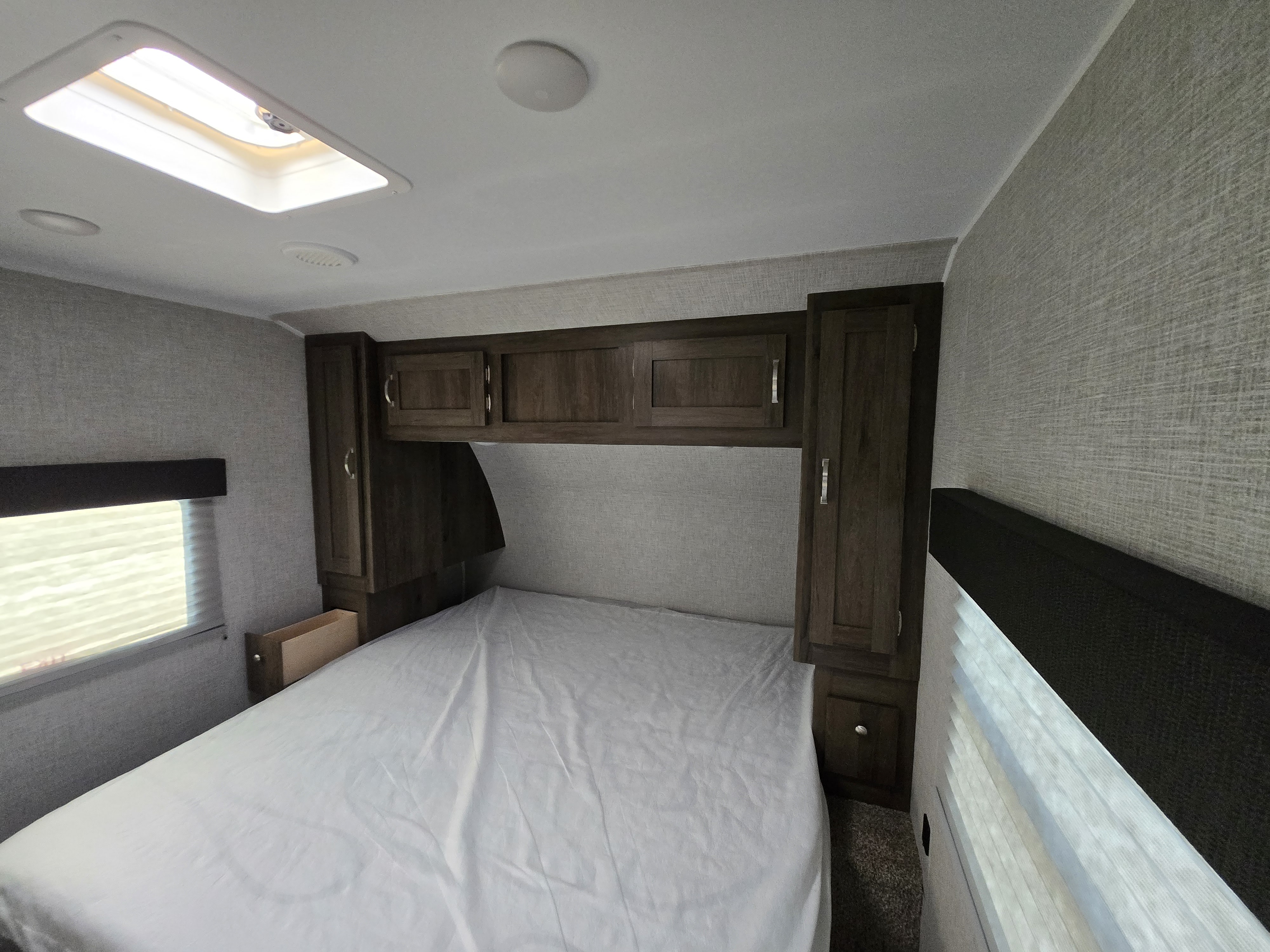Spacious RV rental bedroom with comfortable bed, overhead storage, and natural light from skylight and window.. East to West Della Terra 2021