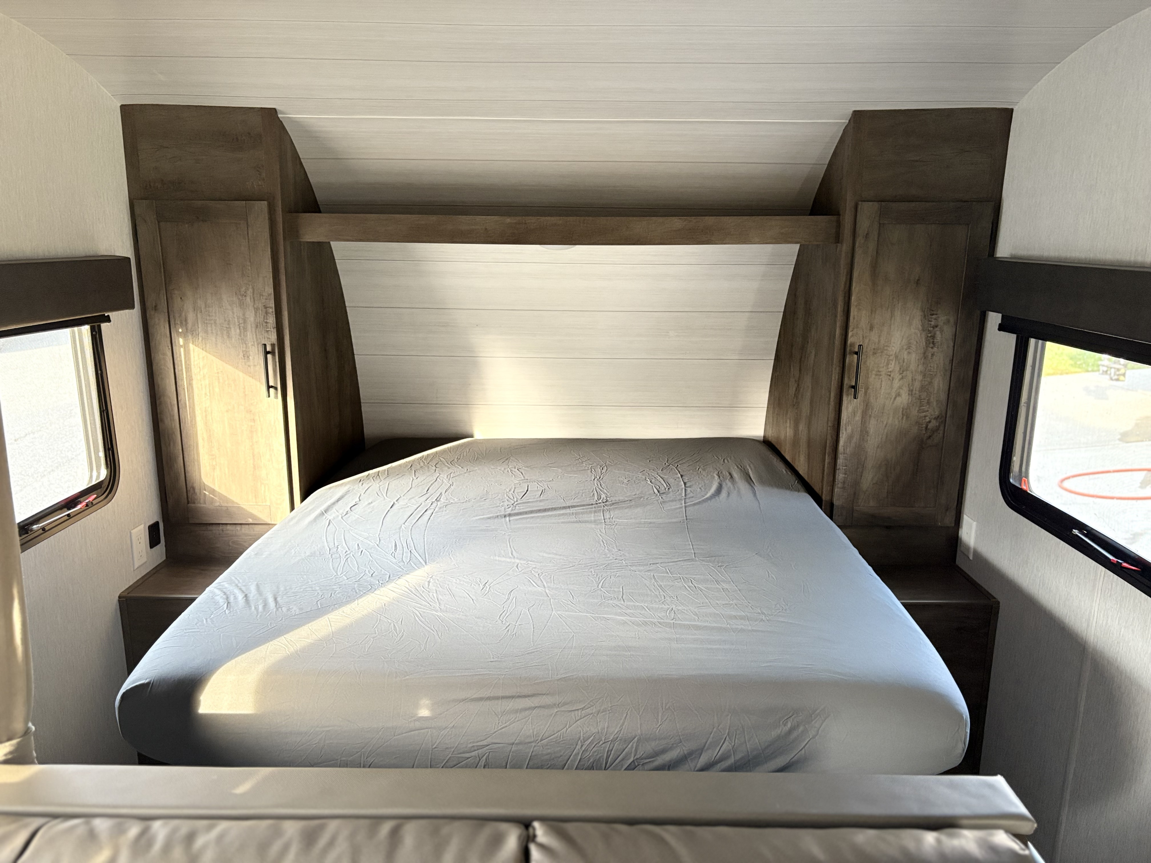 Cozy RV rental bedroom with a bed, built-in cabinets, and windows, ideal for compact living on the go.. Forest River Wildwood X-Lite 2022