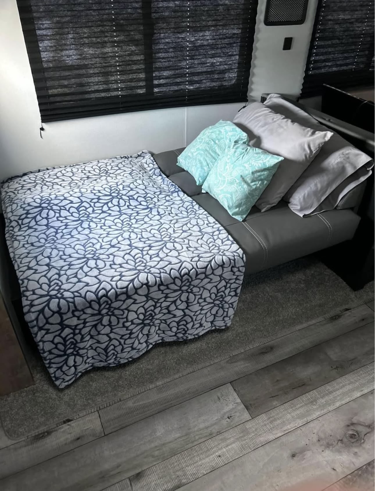 Cozy RV rental living space with a comfy futon, soft floral blanket, and light blue pillows. Ready for relaxation.. Keystone RV Springdale 2022