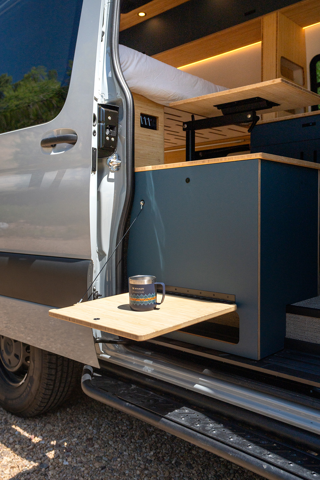 Custom camper van interior for RV rental adventures. Features a cozy bed, pull-out table & clever storage.. Geotrek Albatross Flatiron 2025