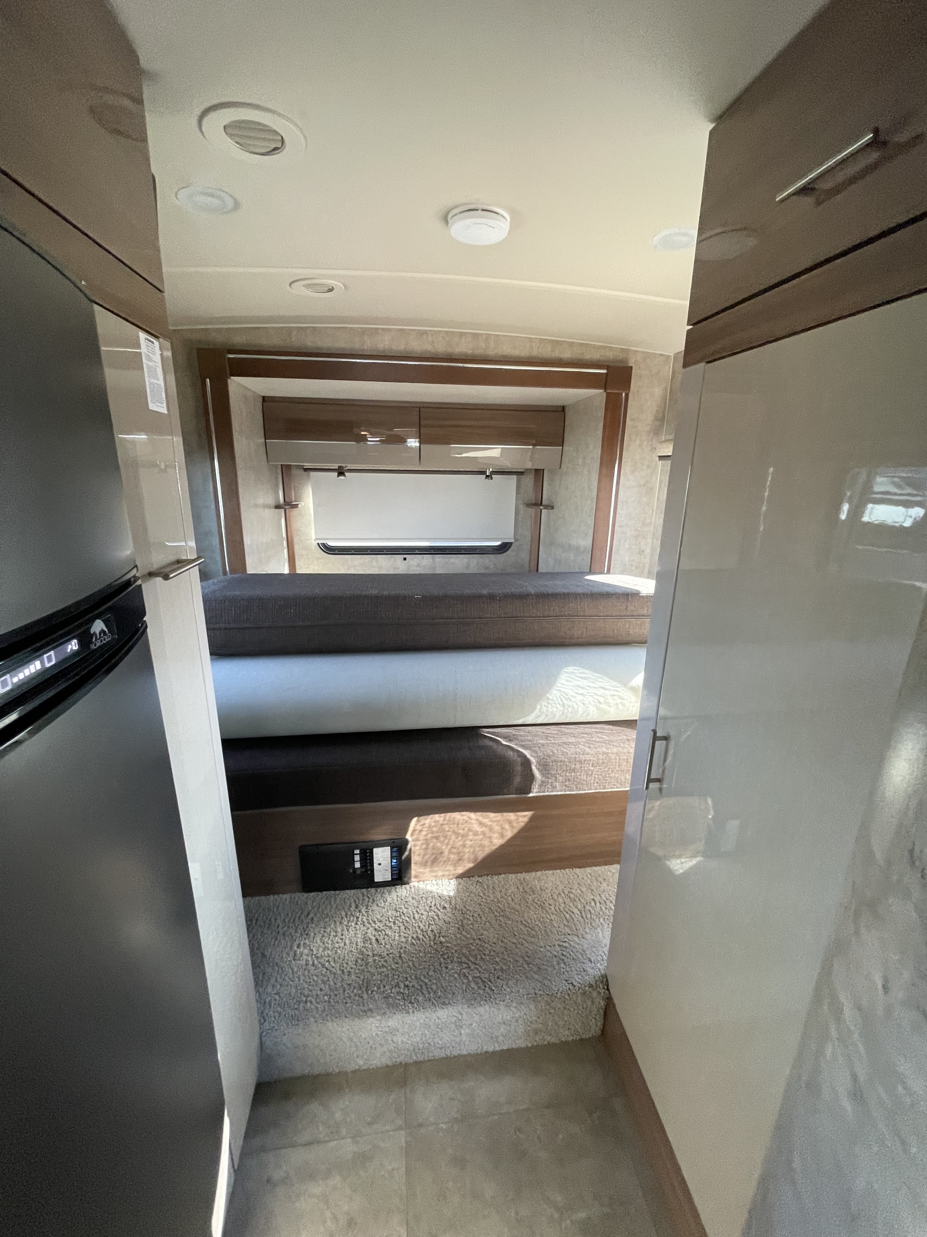 Interior of an RV rental: sleeping area with overhead storage, refrigerator, and control panel visible.. Winnebago View 2015