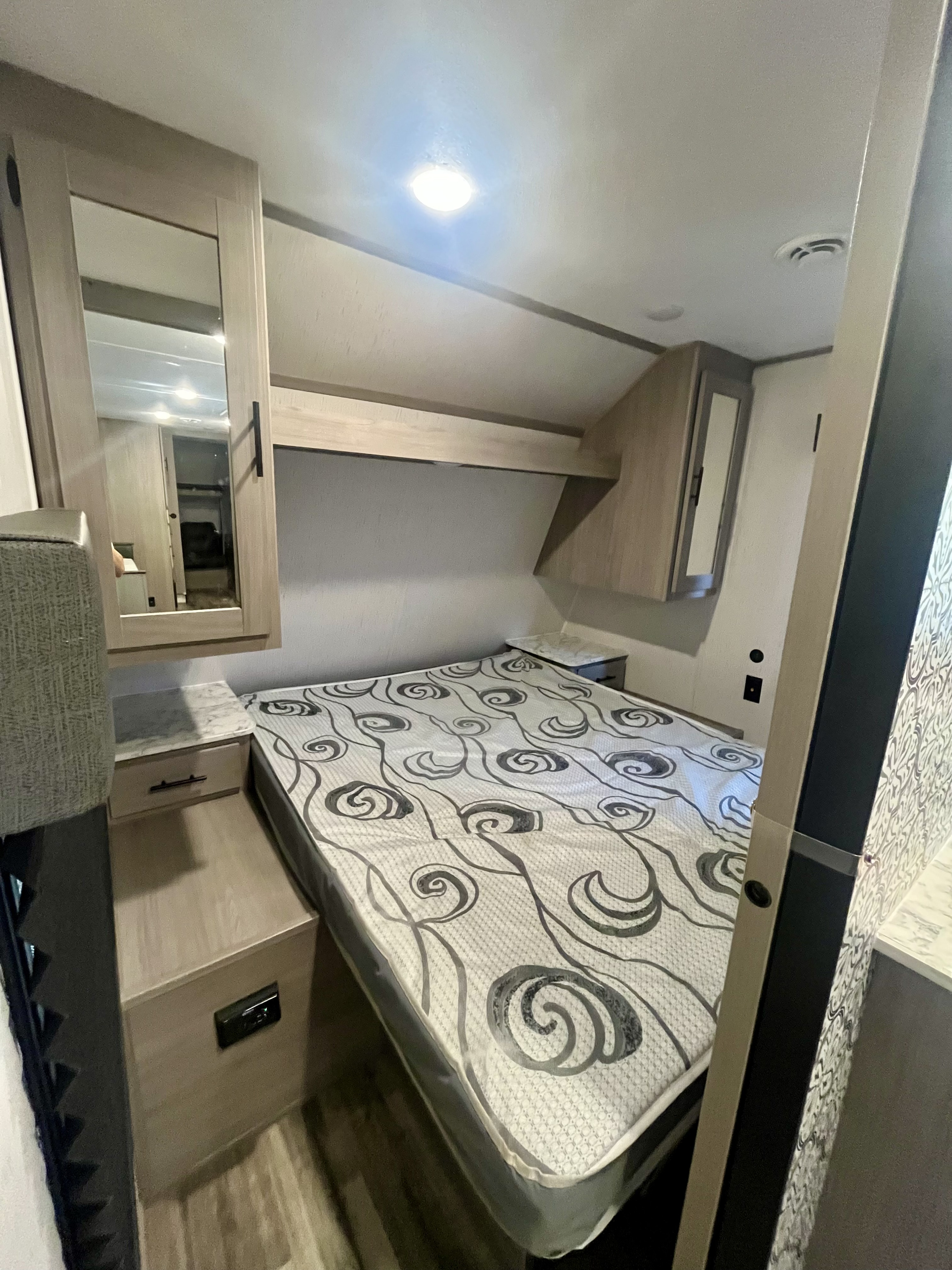 RV rental bedroom featuring a patterned bed, overhead cabinets, and built-in nightstands. Cozy mobile living space.. Dutchmen Coleman Lantern 2023