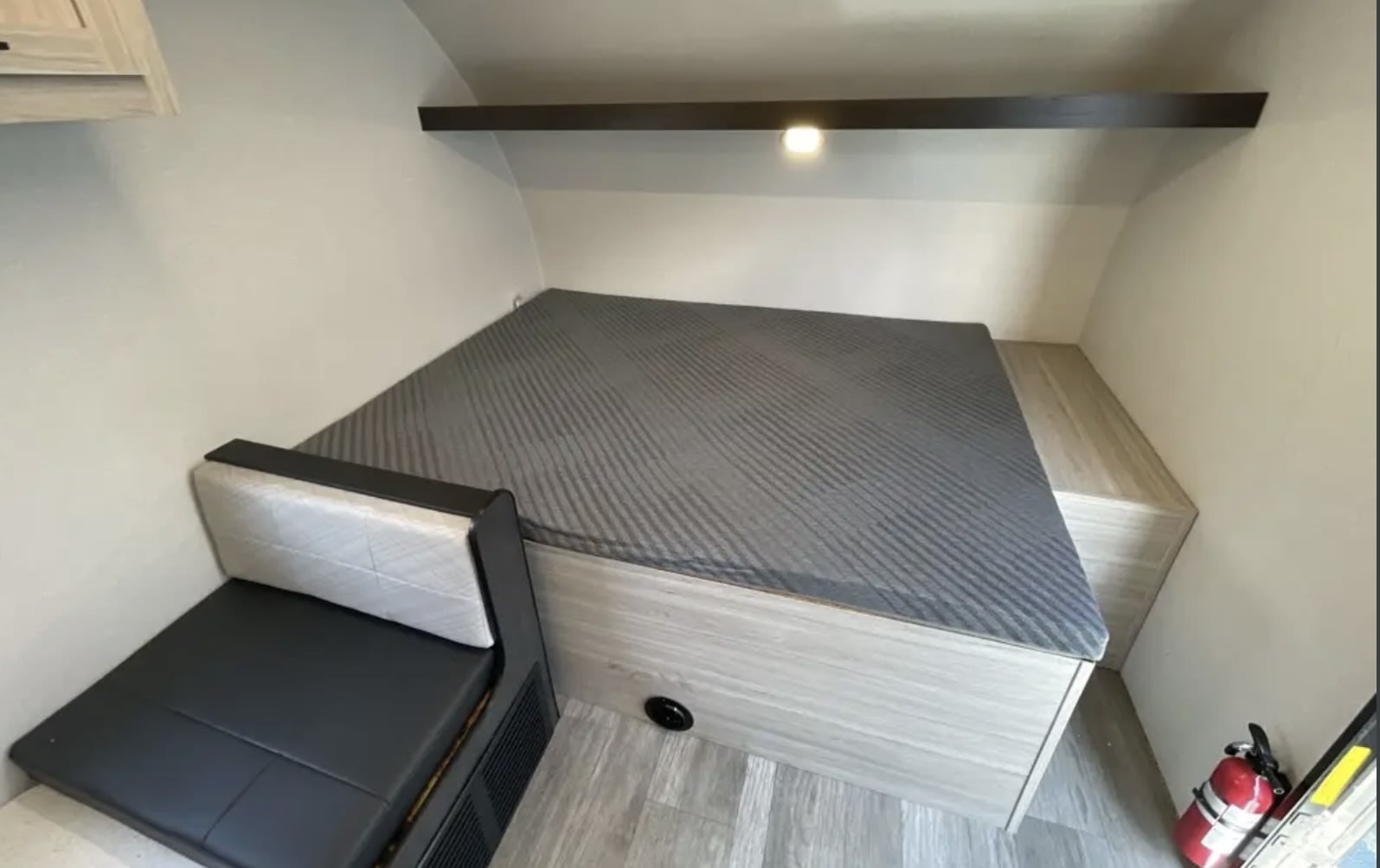 Cozy RV rental interior showcasing a comfortable bed with gray mattress, compact lounge seating, and an overhead shelf.. Heartland Mallard 2025