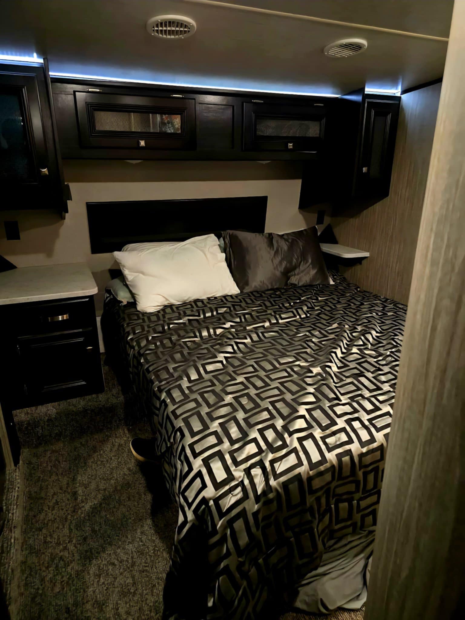 This RV rental bedroom offers comfort: bed with patterned cover, storage cabinets, ambient LED lighting, and nightstand.. Heartland RVs Fuel Toy Hauler 2018