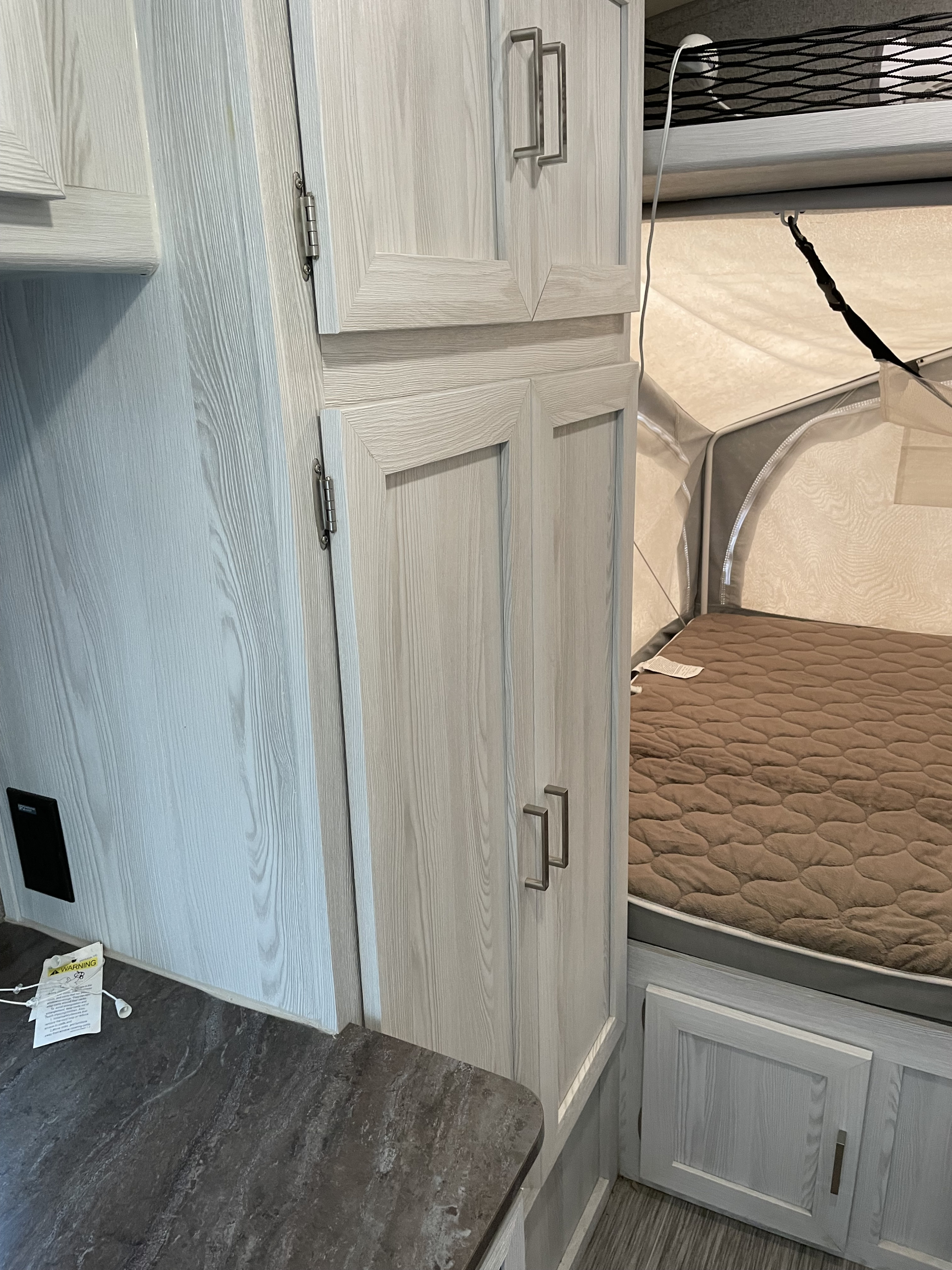 Interior of an RV rental showing light wood cabinets, dark counter, and pop-out bed with quilted mattress.. Forest River Rockwood Geo Pro 2018
