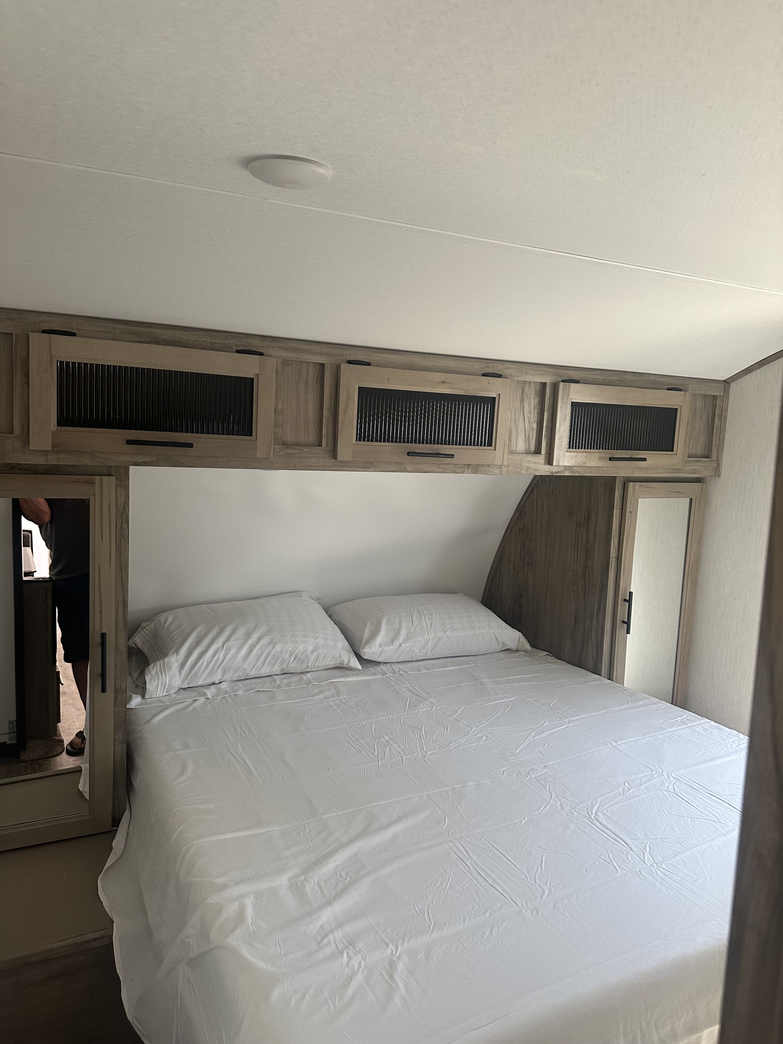 Inside an RV rental bedroom featuring a bed with white linens, overhead cabinets, and mirrored closet doors.. Forest River Cherokee Alpha Wolf 2022