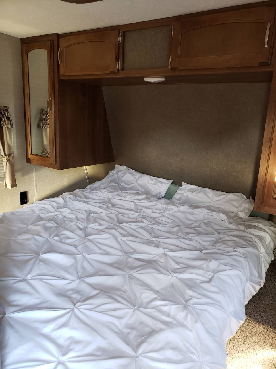 Cozy RV rental bedroom interior with a comfy white comforter, overhead wooden cabinets, and compact built-in storage.. Keystone RV Springdale 2016