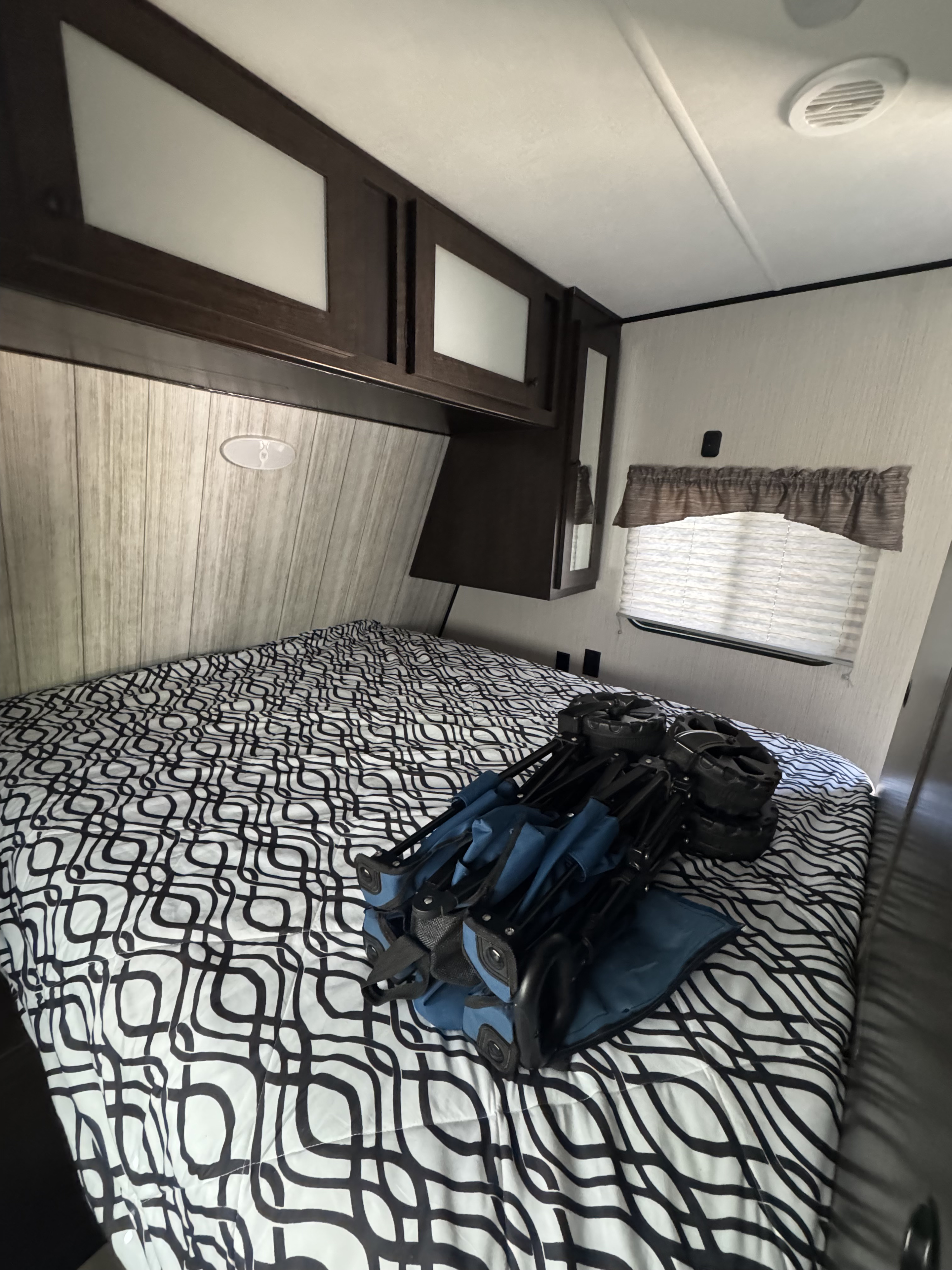 RV rental bedroom with patterned bed, dark wood cabinets, and window. A folded blue wagon is stored on the bed.. Heartland RVs Pioneer 2021