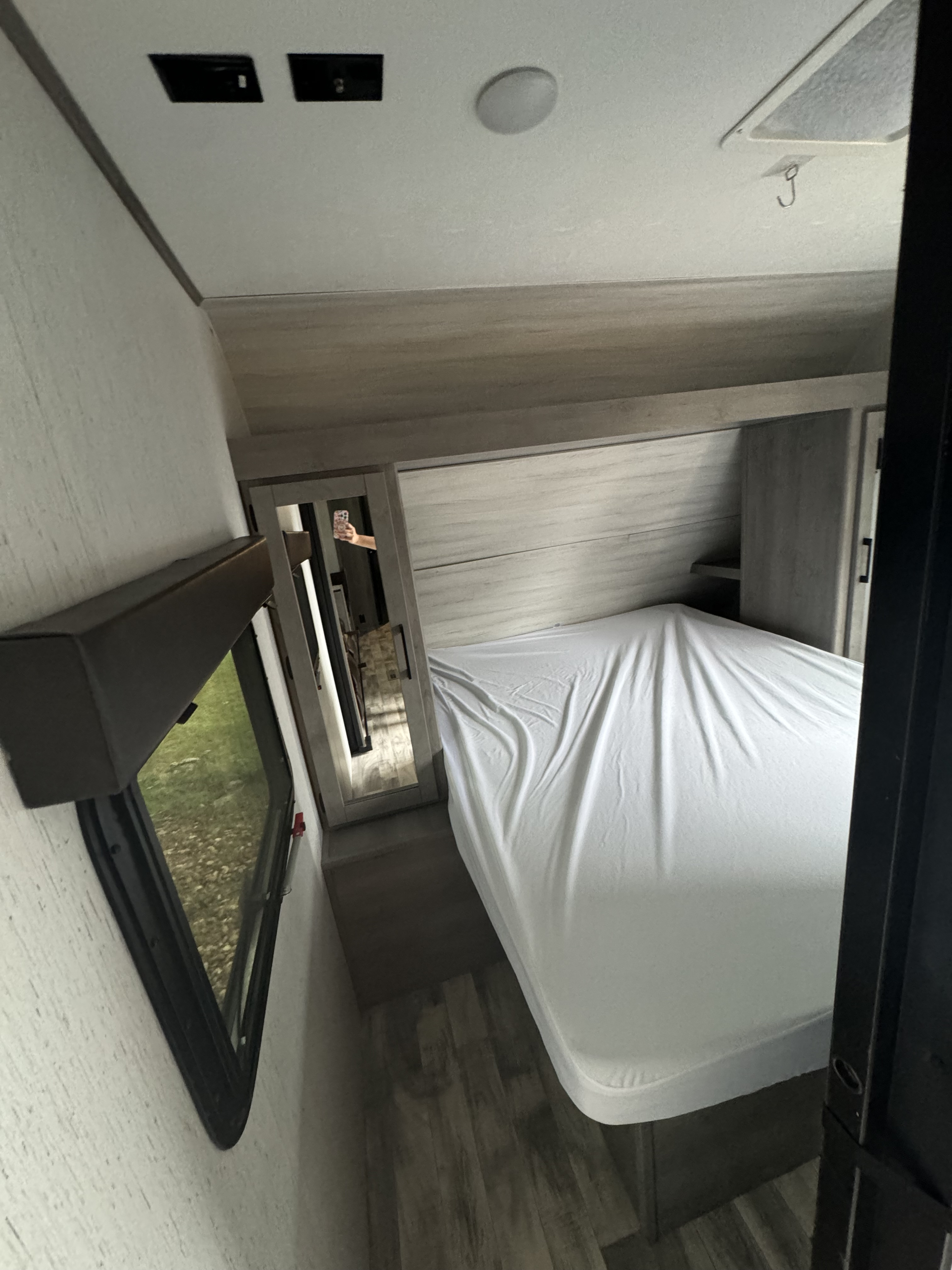 Inside an **rv rental**, a well-lit bedroom features a neatly made bed with white sheets, a window, and overhead fixtures.. Dutchmen Kodiak 2021