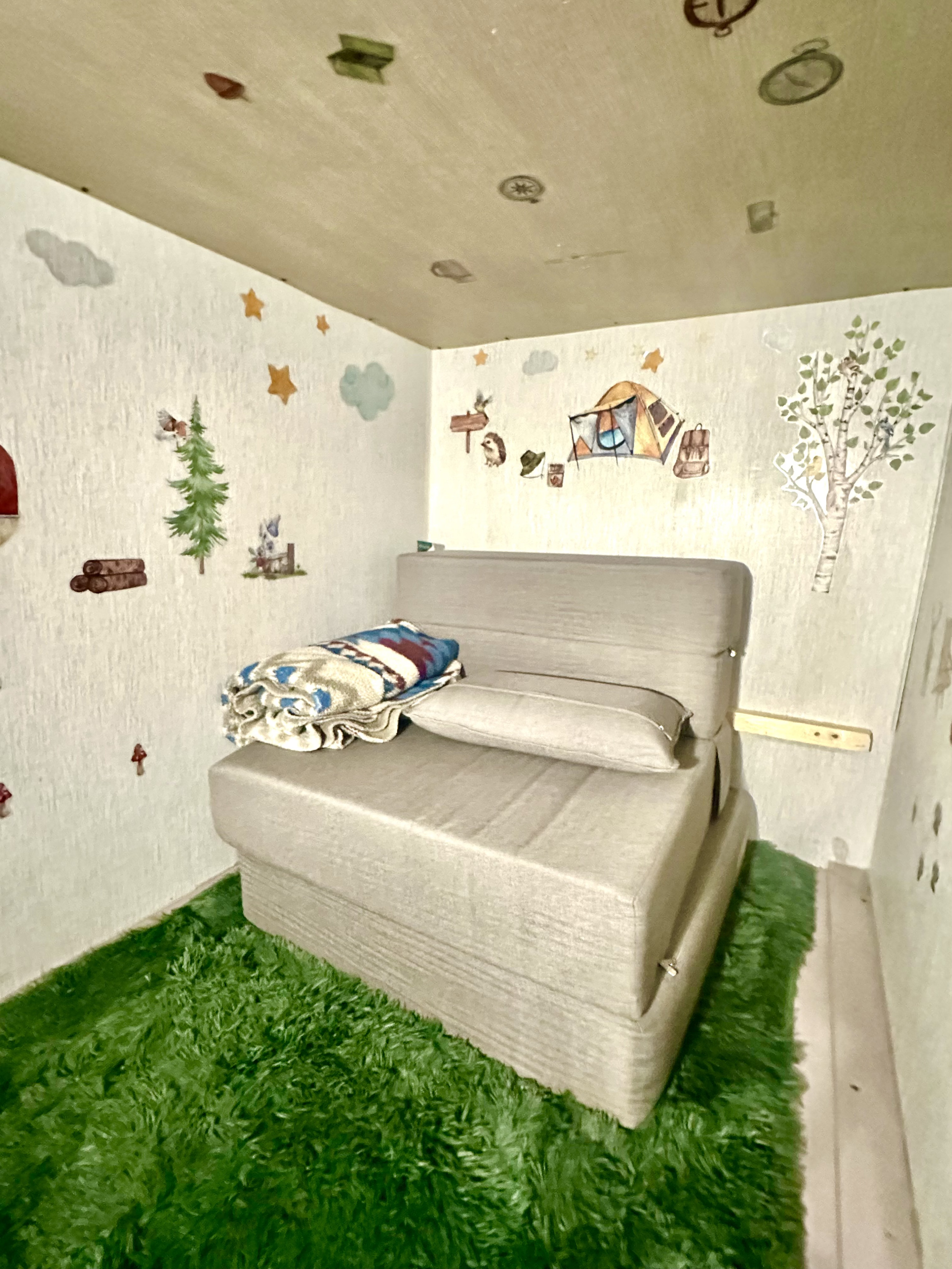 Cozy RV rental sleeping nook with a foldable bed, artificial grass floor, and charming camping-themed decals.. Forest River Wildwood 2023