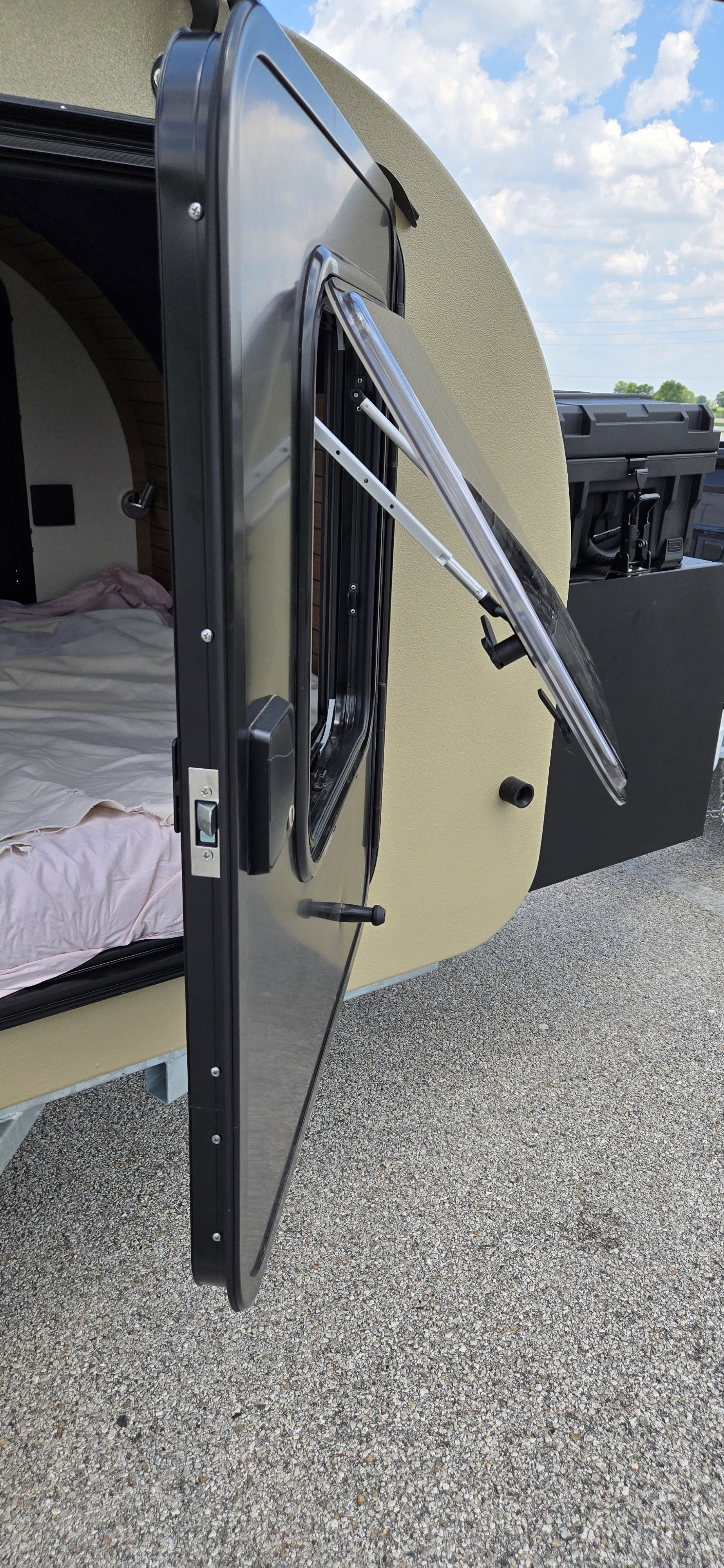 This RV rental shows an open teardrop camper door, revealing a comfy bed and an open window, perfect for camping travel.. Cedar Ridge Camper Vega 2.0 AT 2025
