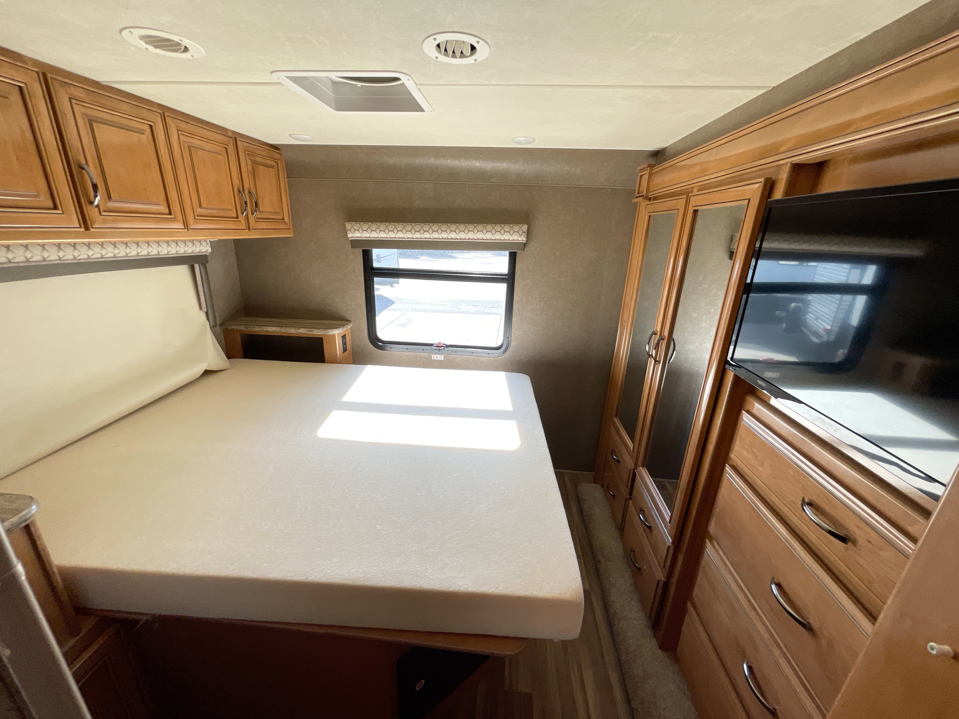 RV rental shows a cozy bedroom with a bed, TV, and cabinets, ideal for a comfortable stay on your next adventure.. Thor Quantum 2018