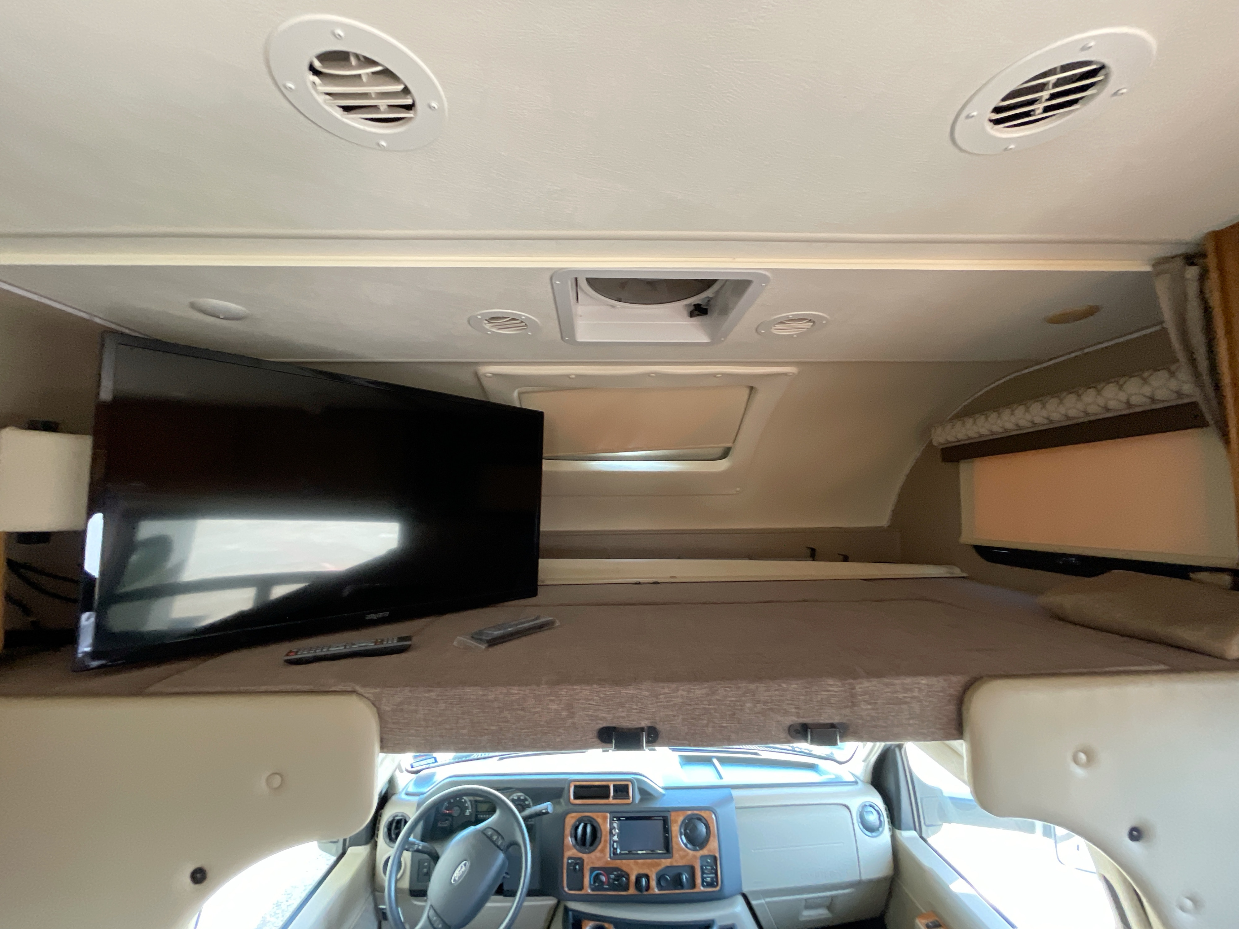 RV rental interior: over-cab bunk bed with TV, ceiling vents, and front dashboard view. Great for travel adventures.. Thor Quantum 2018