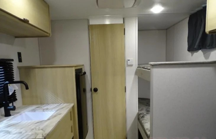 Interior of an RV rental, featuring a kitchen area with a sink, a door, and built-in bunk beds for travelers.. Forest River Wildwood FSX 174BHLE 2024