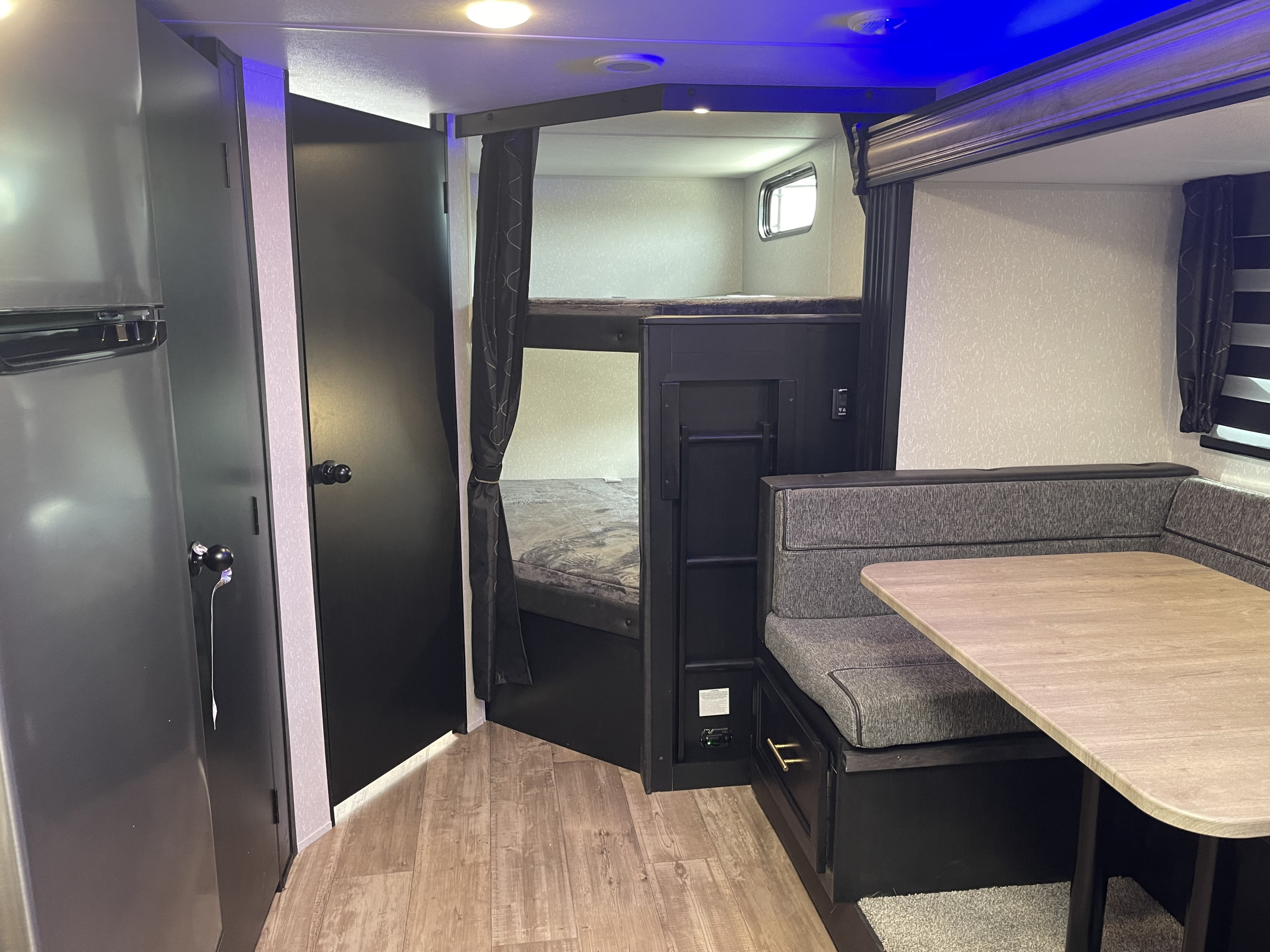 RV rental interior view: bunk beds, a dinette, and refrigerator, all in a compact layout with ambient blue and white lighting.. Forest River Cherokee 2022