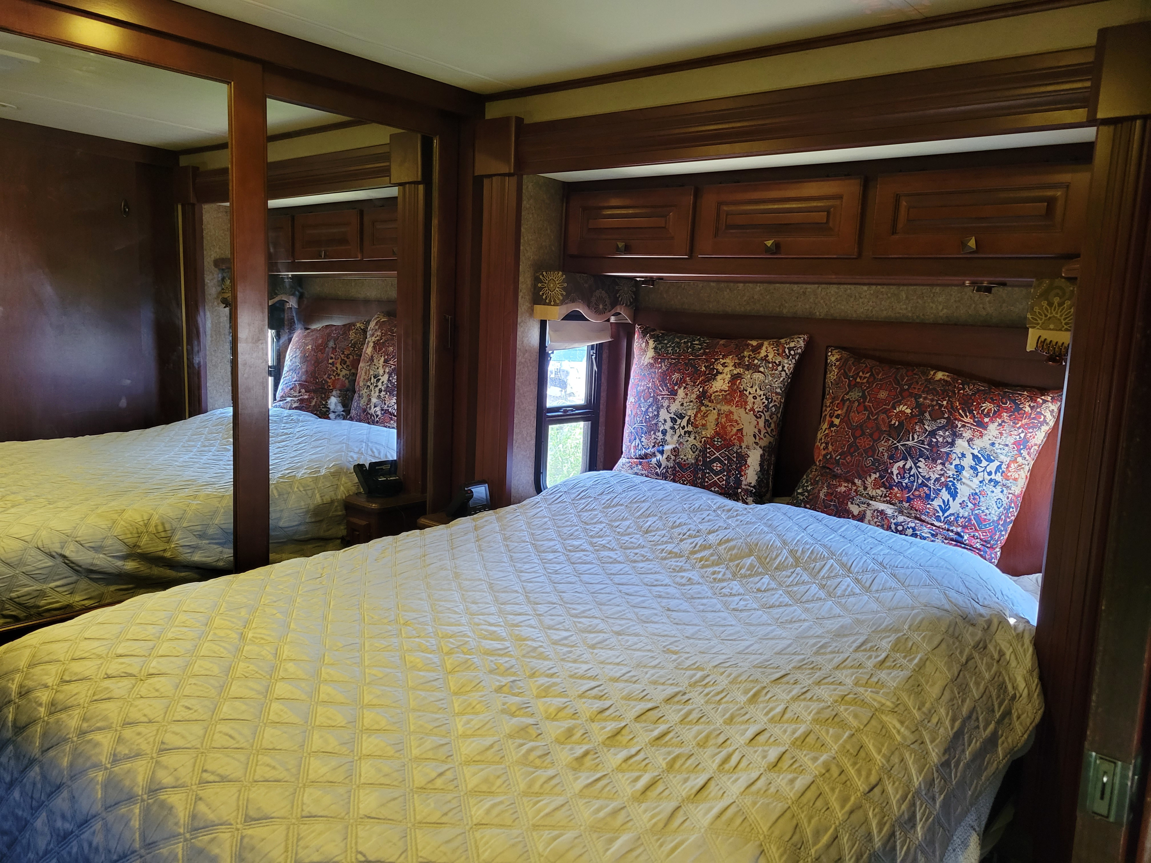 A comfortable RV rental bedroom featuring a queen bed with patterned pillows, overhead cabinets, and a mirrored closet.. Forest River Berkshire 390-Bunkhouse 2012