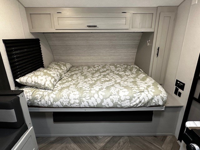 RV rental bedroom: A cozy bed with a green leaf-patterned comforter, pillow, overhead cabinets, and a wardrobe offer compact comfort.. Forest River Salem FSX 2022