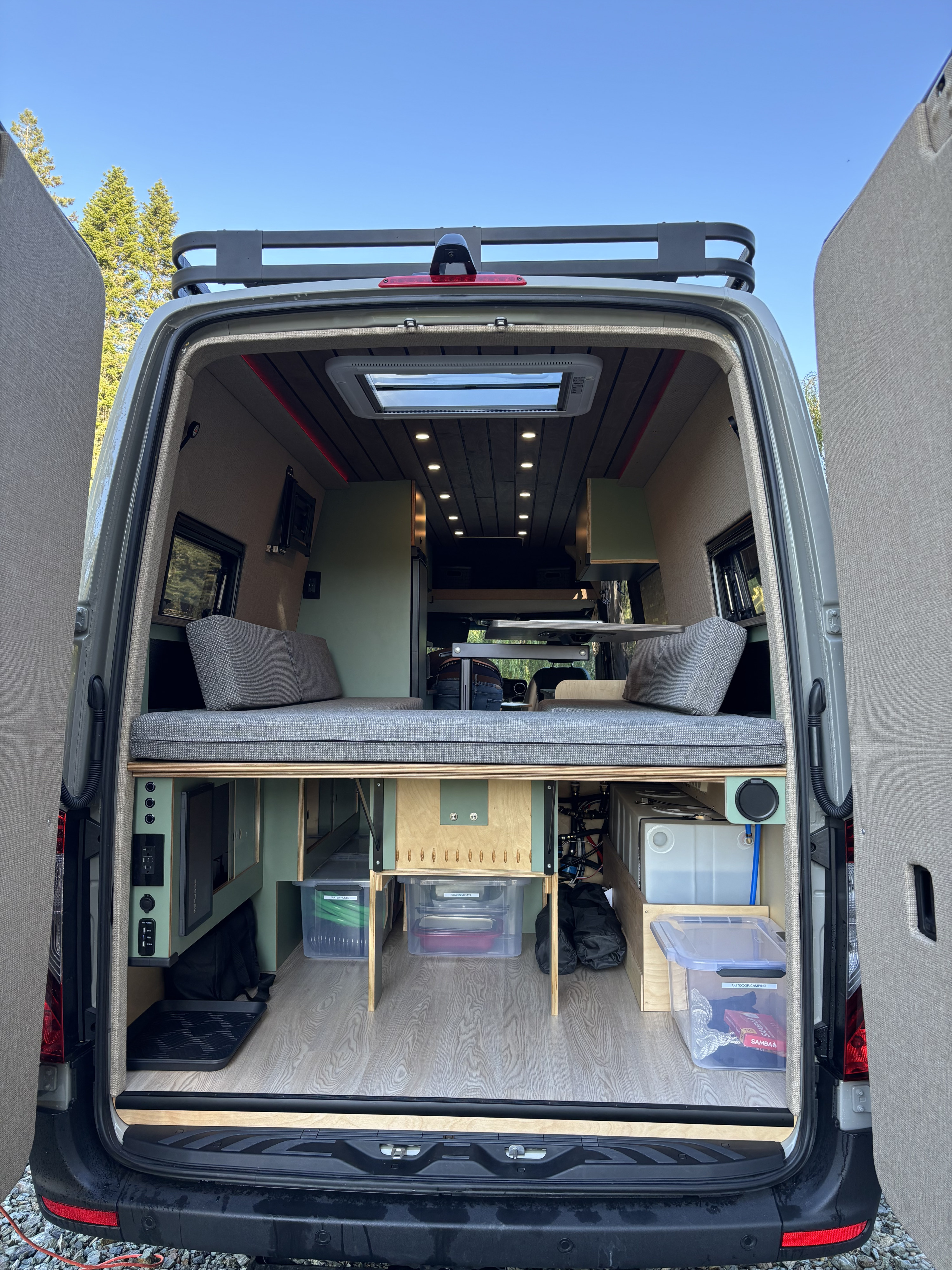 Inside a modern **rv rental**: back doors open to a custom camper van interior with raised bed, abundant storage & utility.. Mercedes-Benz Sprinter 2025