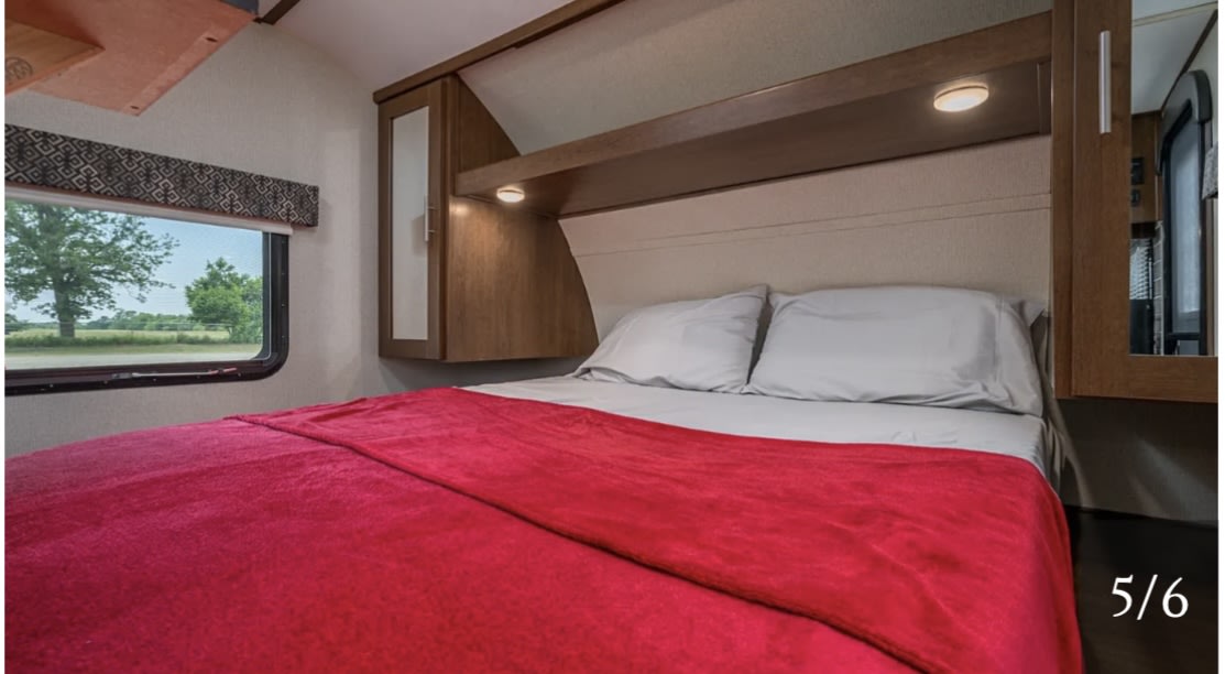 Inviting RV bedroom for your rv rental. Features a comfy bed, red blanket, ample storage, and a window with a countryside view.. Forest River Impression 2019