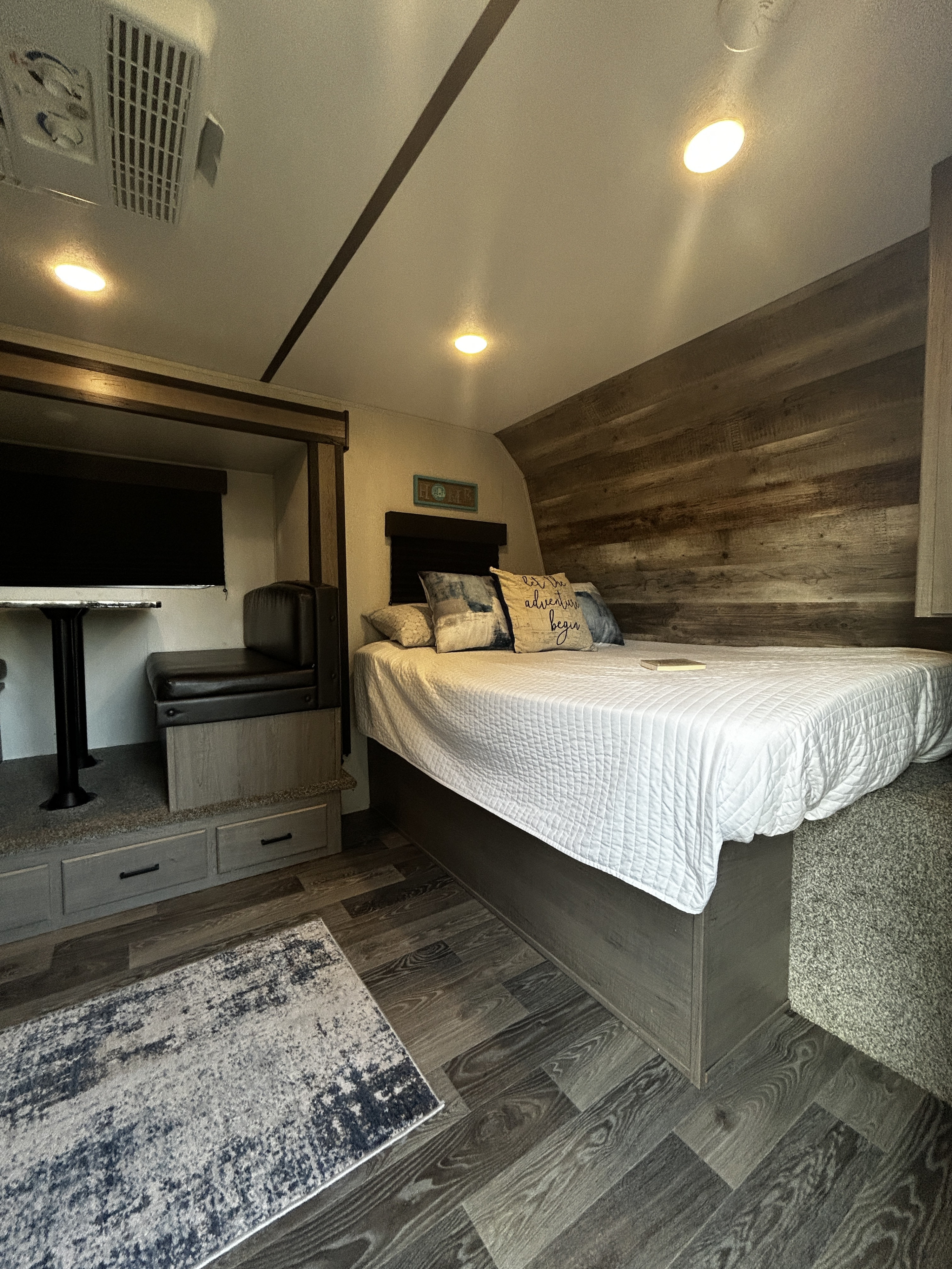 Cozy RV rental interior with a comfortable bedroom, rustic wood paneling, and a clever dinette with built-in storage.. Keystone RV Hideout 2021
