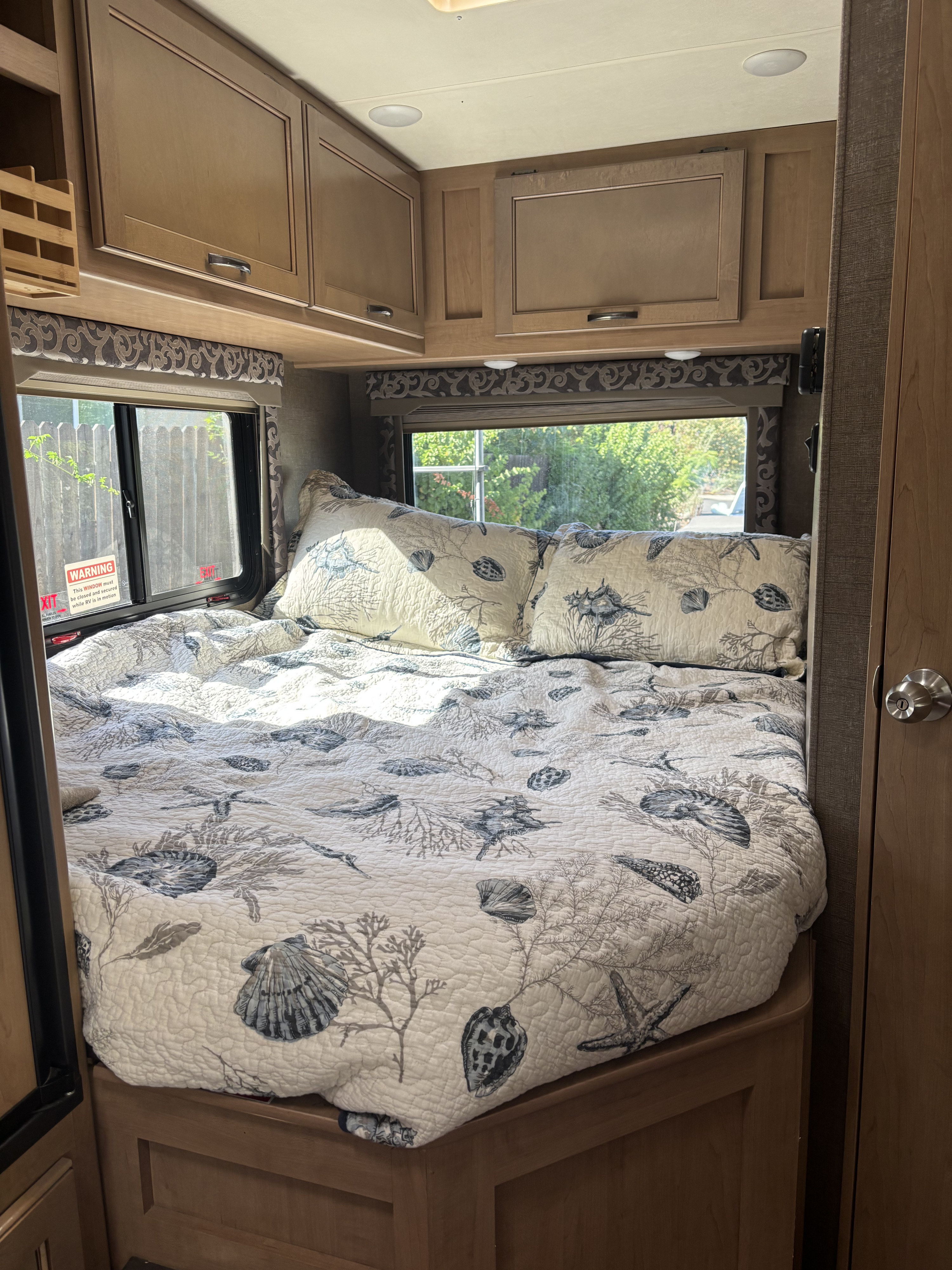 Bright and inviting RV rental bedroom with a comfortable bed, sea-themed quilt, overhead cabinets, and windows offering outdoor views.. Thor Four Winds 2020
