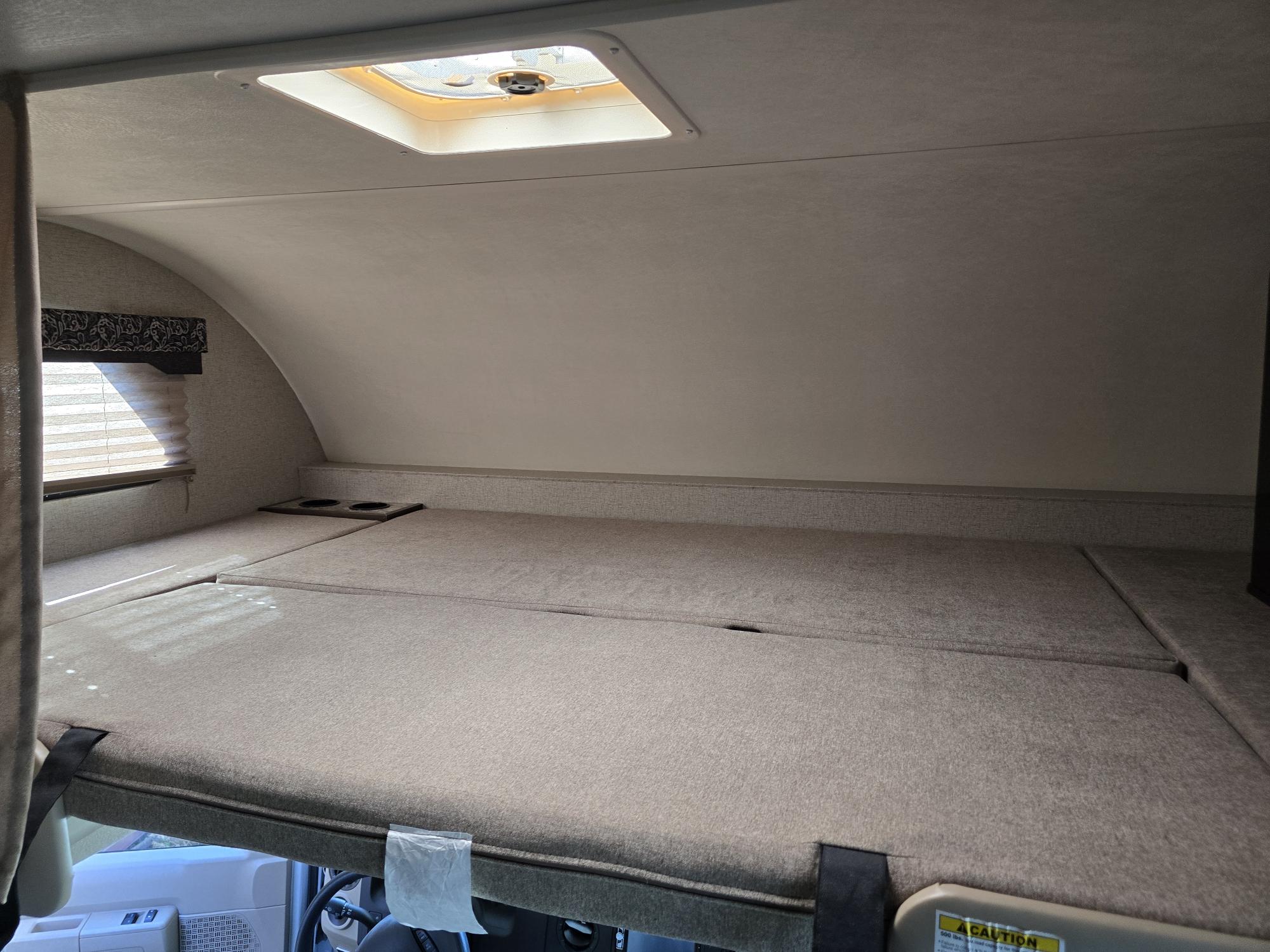 Spacious over-cab bunk bed in an rv rental, perfect for extra sleeping space. Features a window, skylight, and cup holders.. Thor Freedom Elite 2020