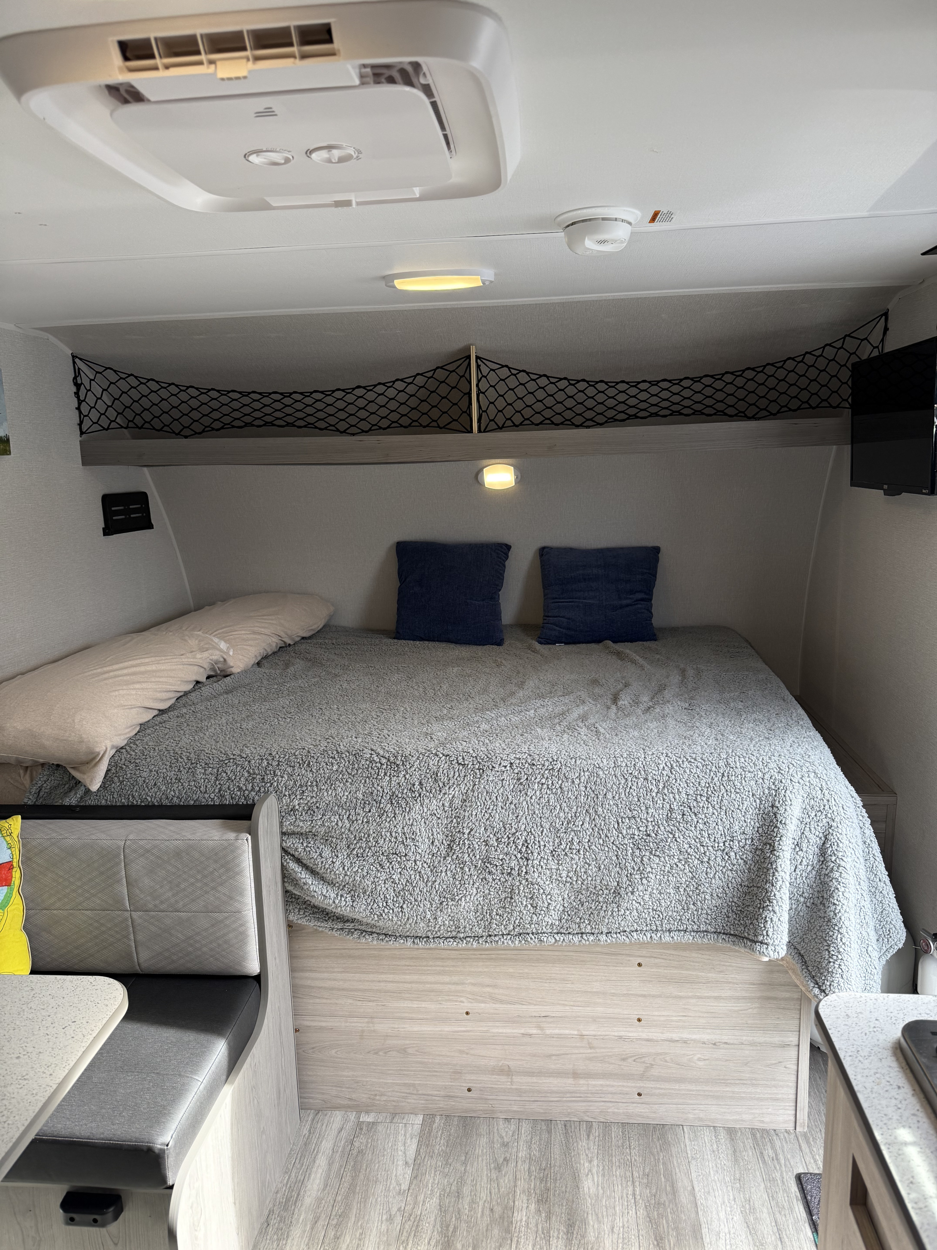 Cozy RV rental interior featuring a comfortable bed with grey blanket, overhead storage net, and dinette area.. Heartland Pioneer 2025