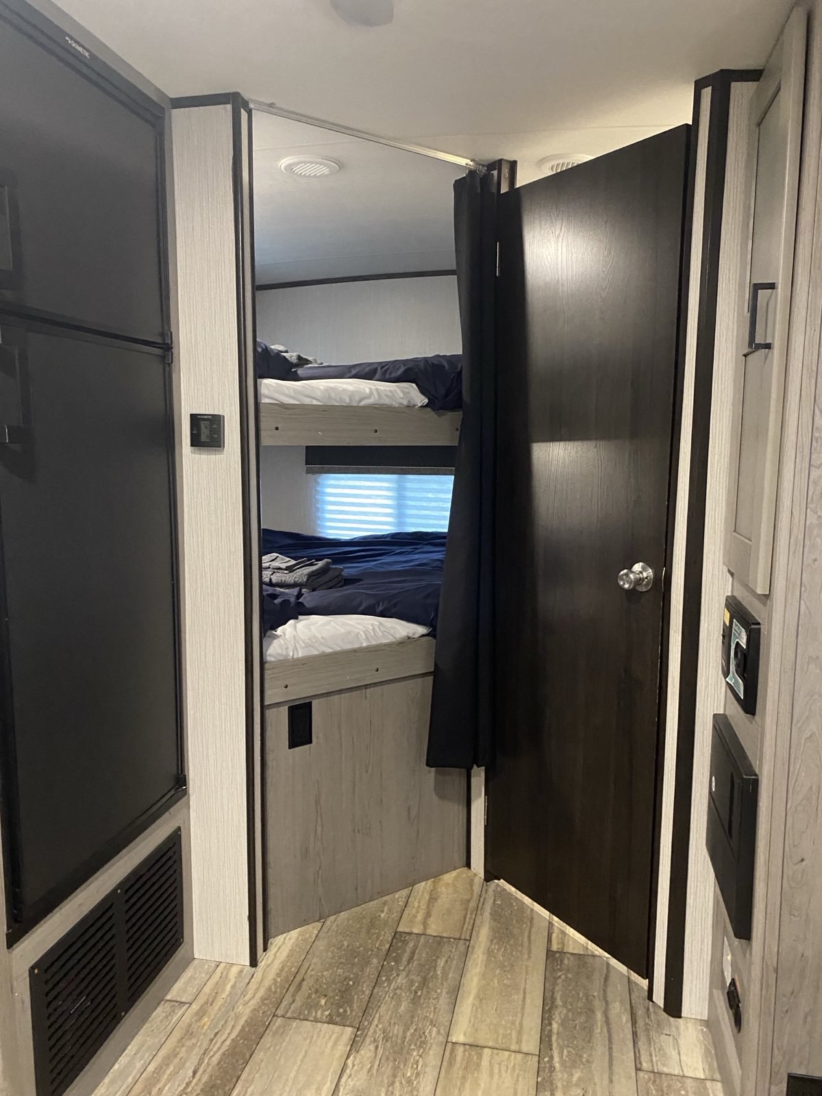 Experience RV rental comfort: A view of bunk beds with dark bedding, a wooden floor, and an adjacent fridge in a modern RV.. Heartland RVs North Trail 2021
