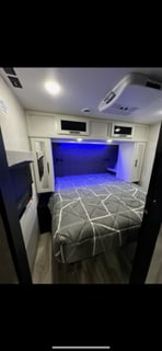 Cozy RV rental bedroom featuring a modern patterned bed, ambient blue lighting, built-in storage, and TV. Ideal travel accommodation.. Crossroads RV Cruiser aire CR28BBH24 2024