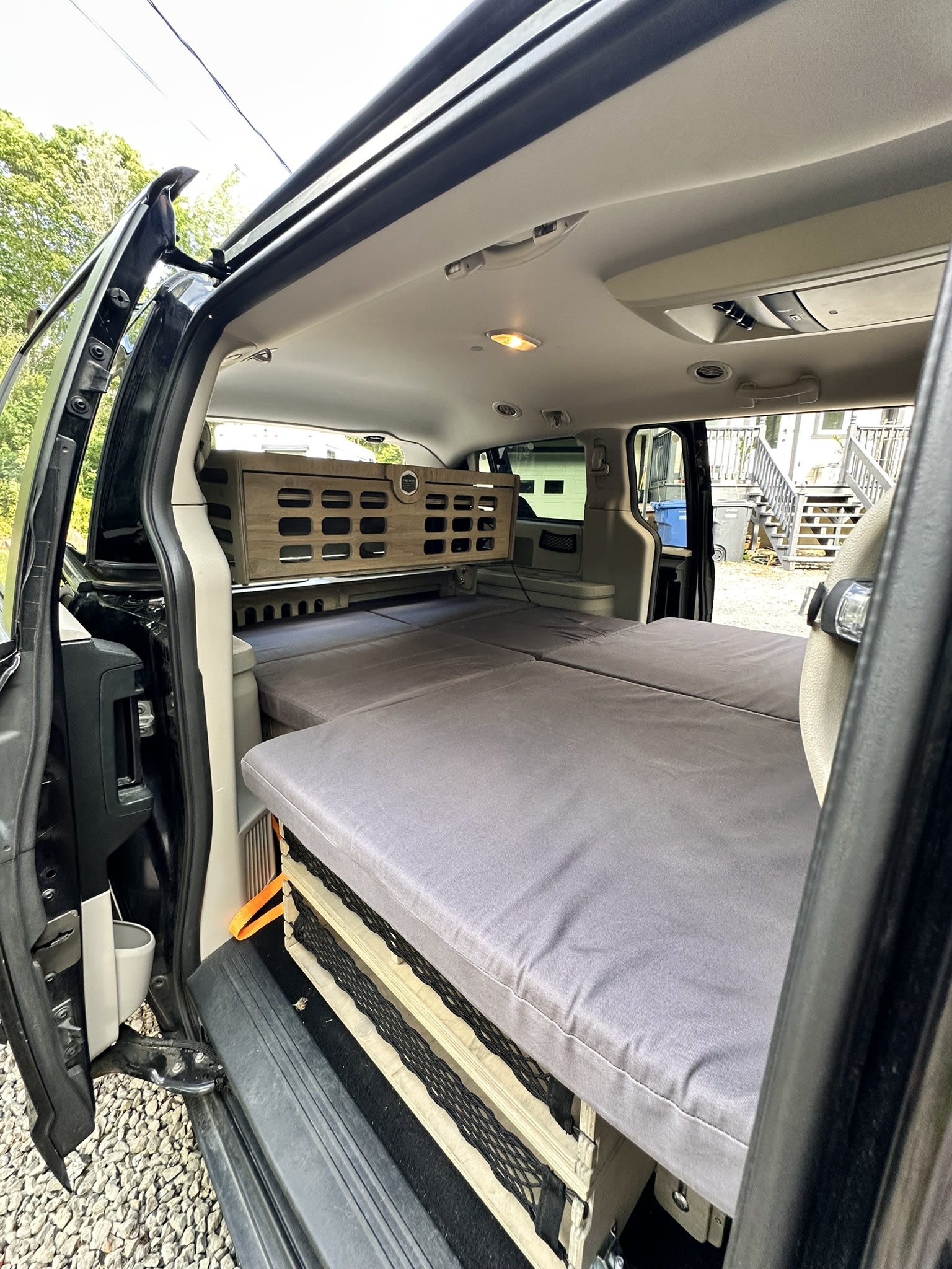 View inside an RV rental minivan camper. It features a custom bed system with gray mattresses & overhead wooden storage.. Dodge Grand Caravan 2012
