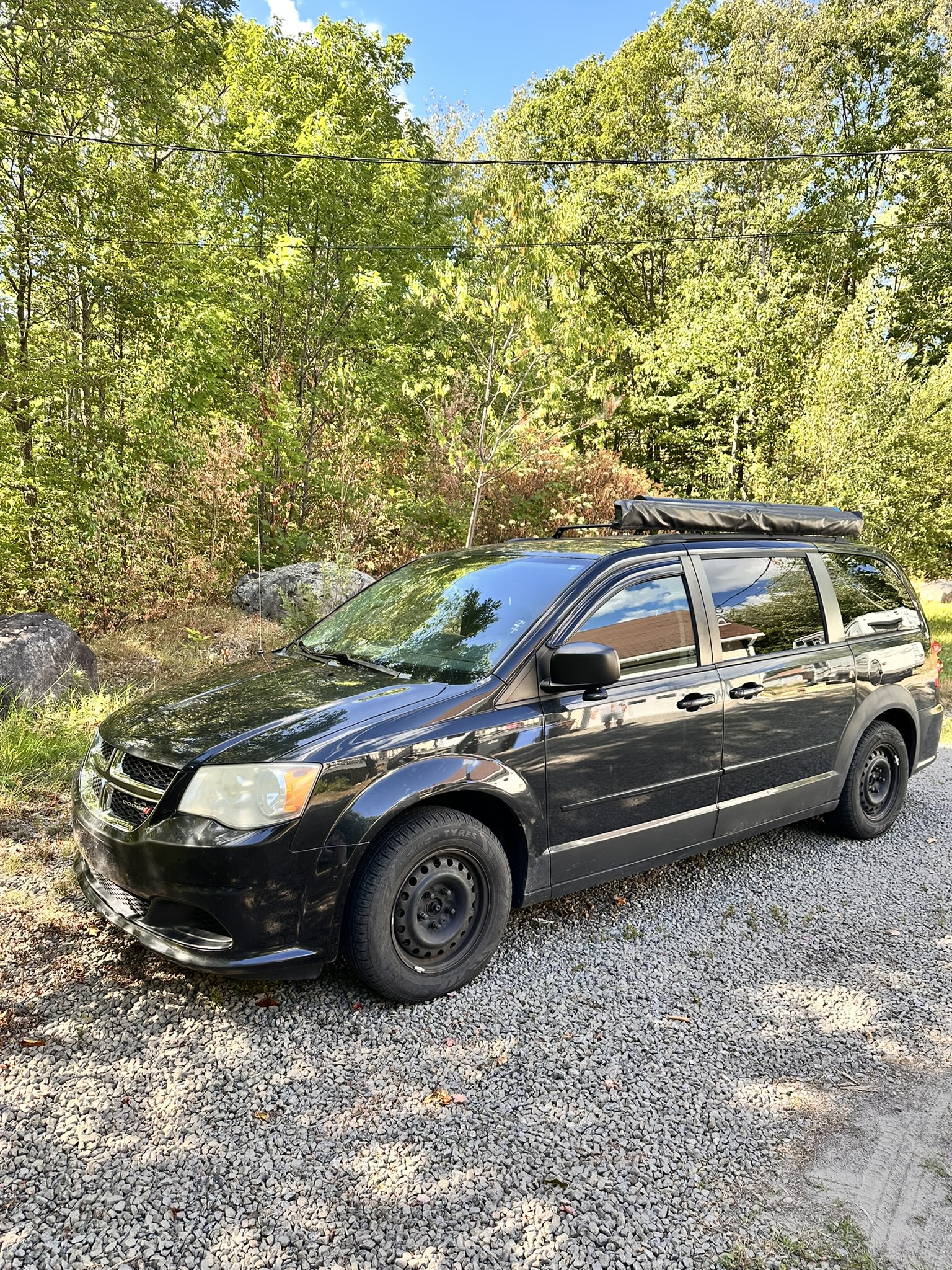 Black customized minivan on gravel, ready for adventure. A great option for compact RV rental.. Dodge Grand Caravan 2012