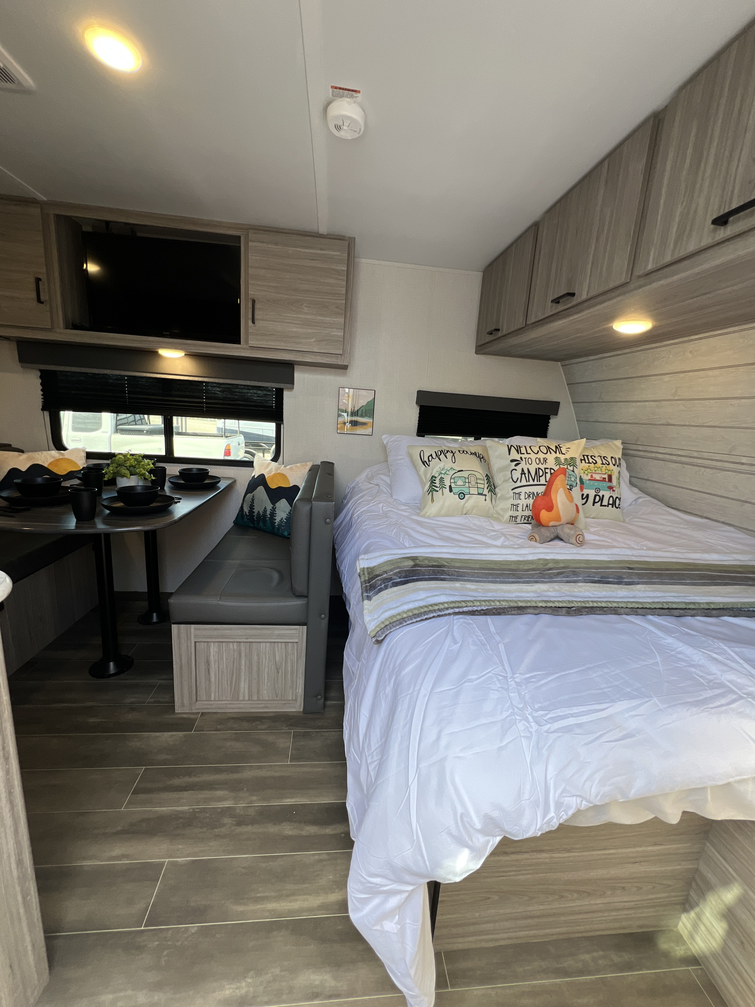 Inside a stylish rv rental: a compact dining booth, cozy bed with fun camping pillows, and sleek overhead cabinets.. Keystone RV Passport SL Ultra Lite 2024