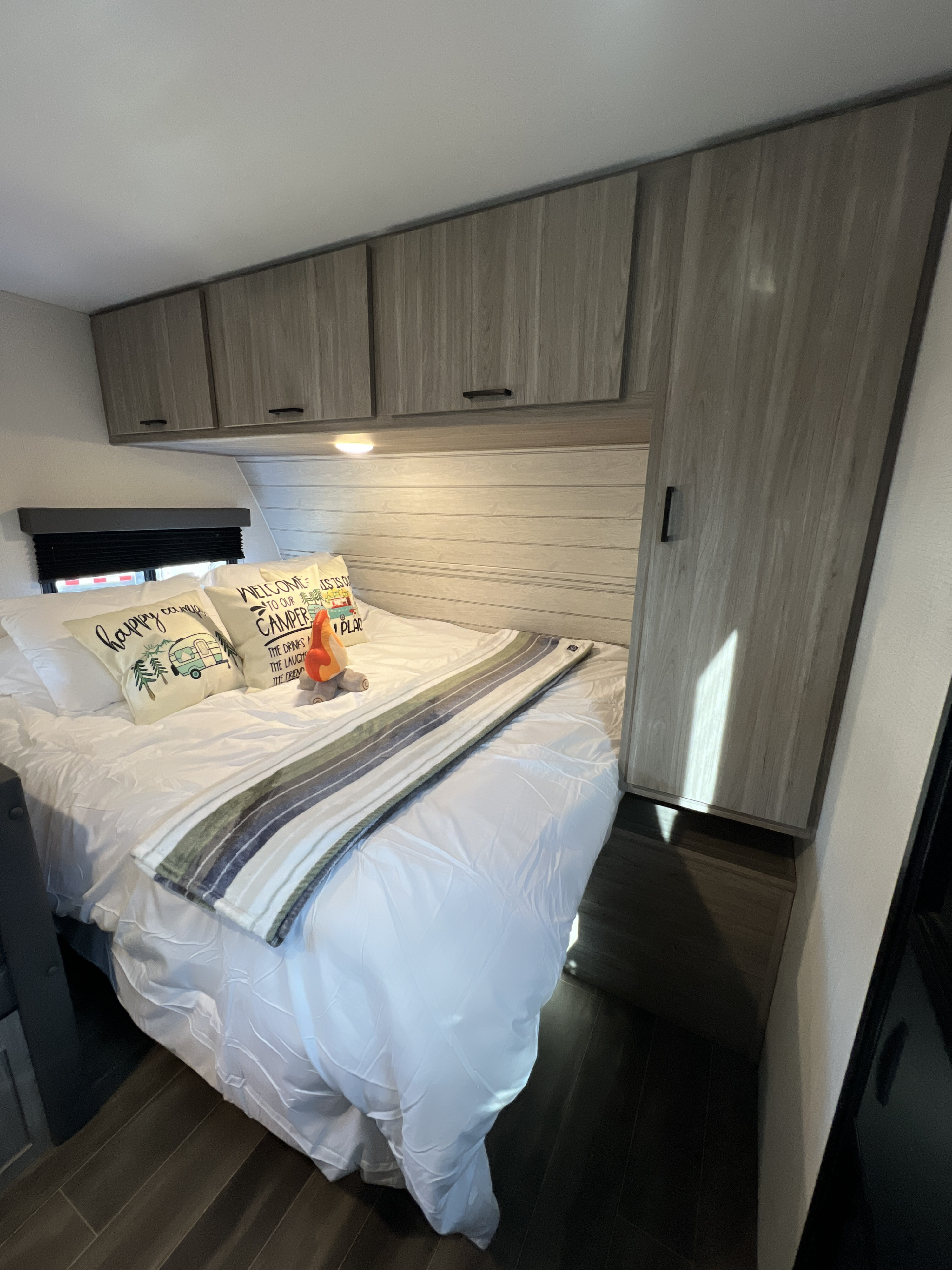 Cozy RV rental bedroom features a comfortable bed, camper-themed pillows, and ample overhead storage. Ready for your adventure!. Keystone RV Passport SL Ultra Lite 2024