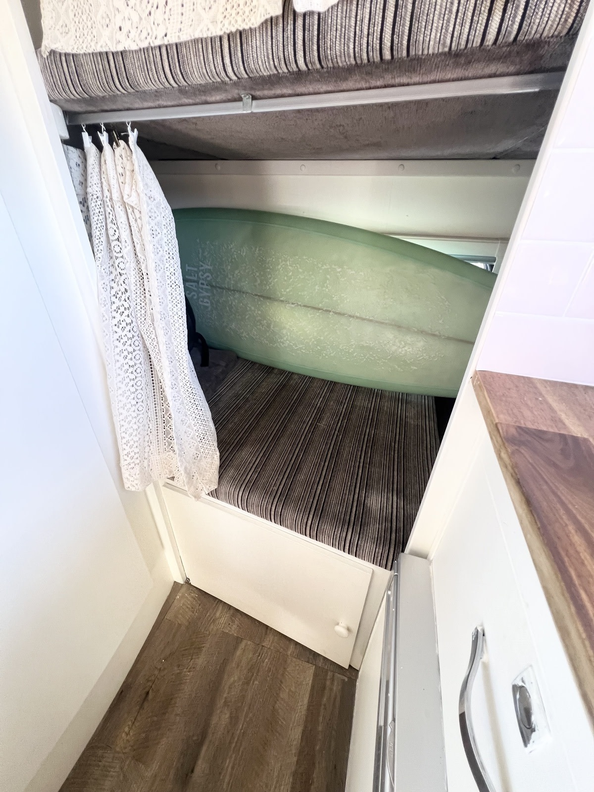 RV rental interior featuring compact bed with striped cushion, surfboard storage, and lace privacy curtain.. Toyota Camroad 2015
