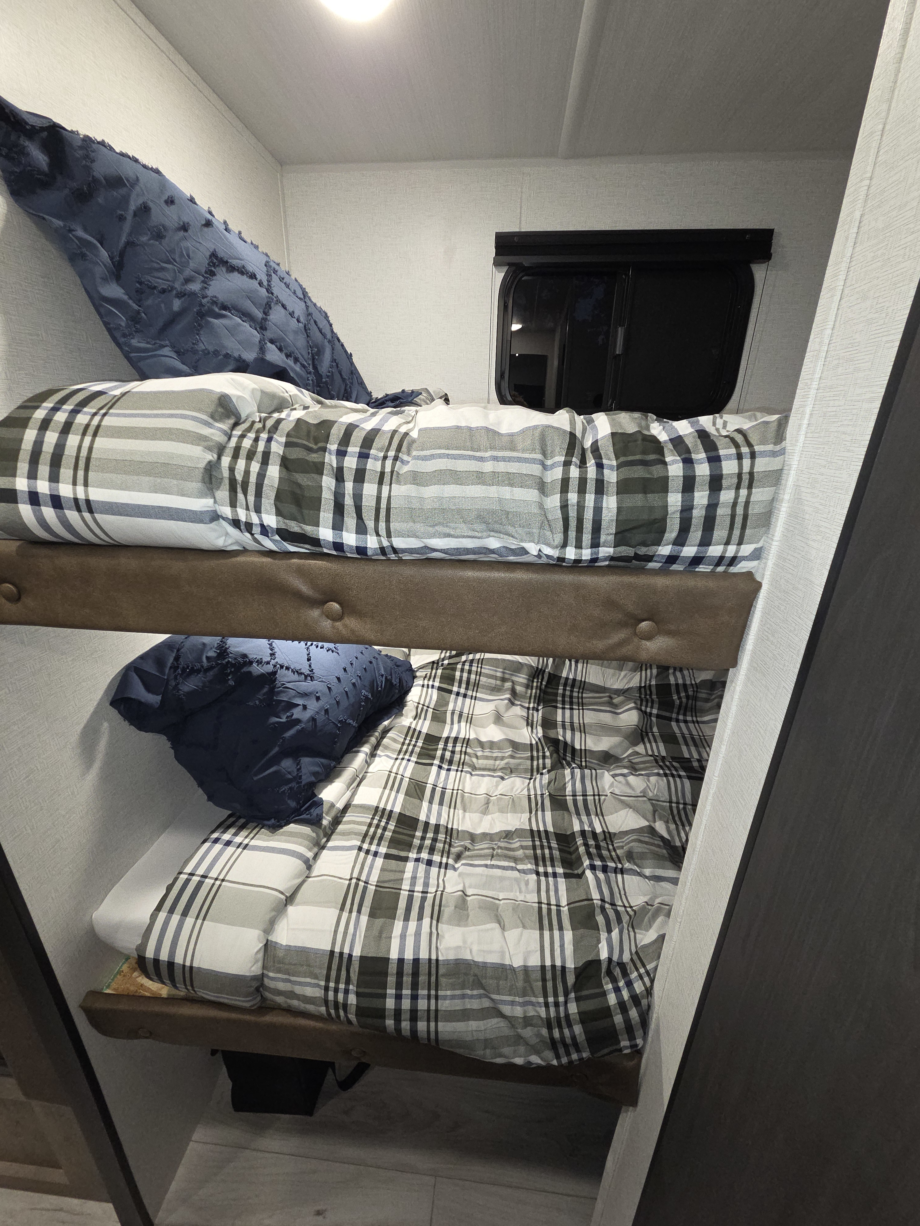 Comfortable bunk beds in an RV rental, featuring cozy plaid comforters and blue pillows, ideal for compact sleeping.. Keystone Springdale West BHWE 2025