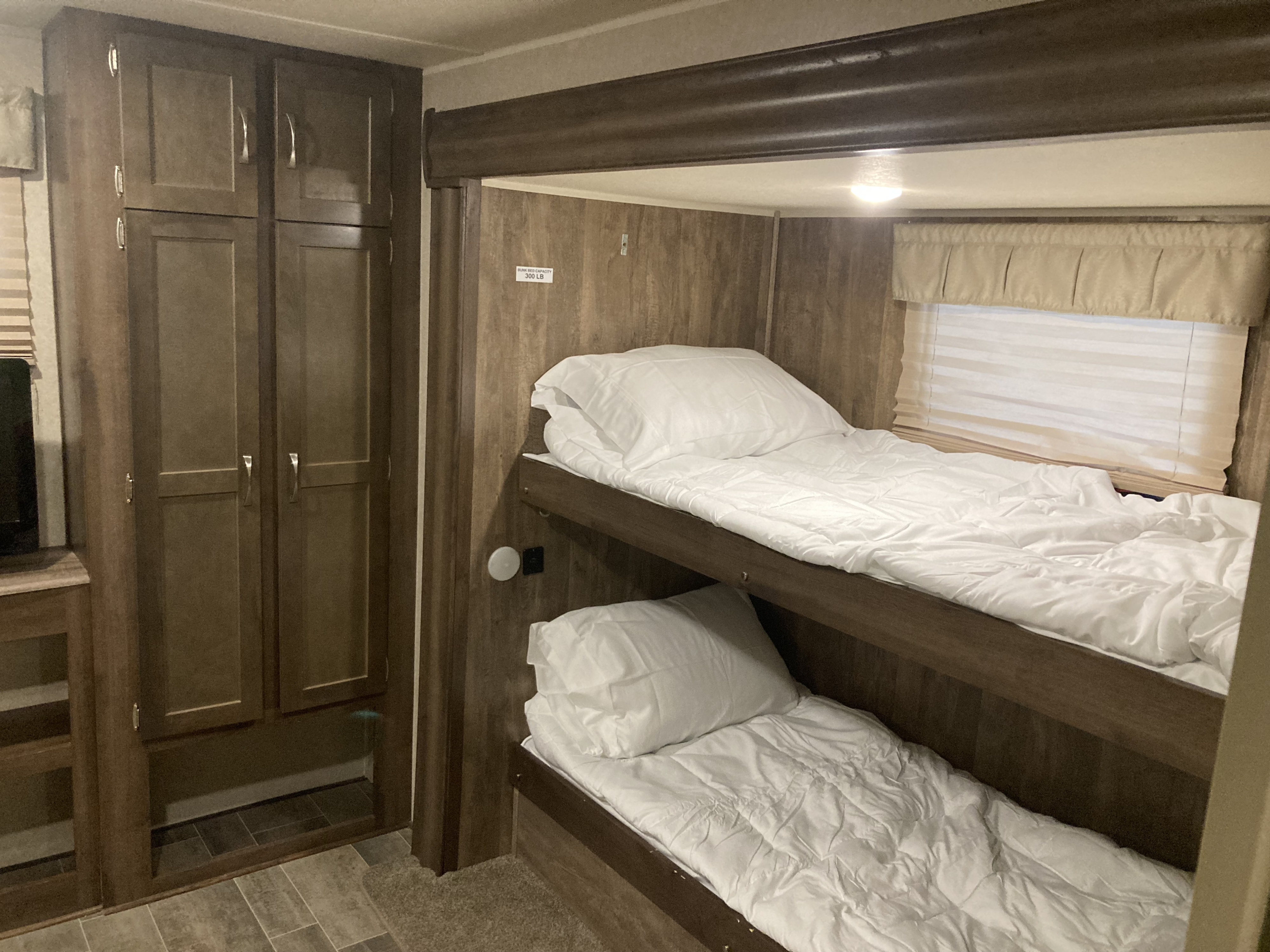 RV rental bunk beds with white bedding, a wardrobe, and window blinds offer comfy sleep. Capacity 300lb.. Palomino Puma 2020