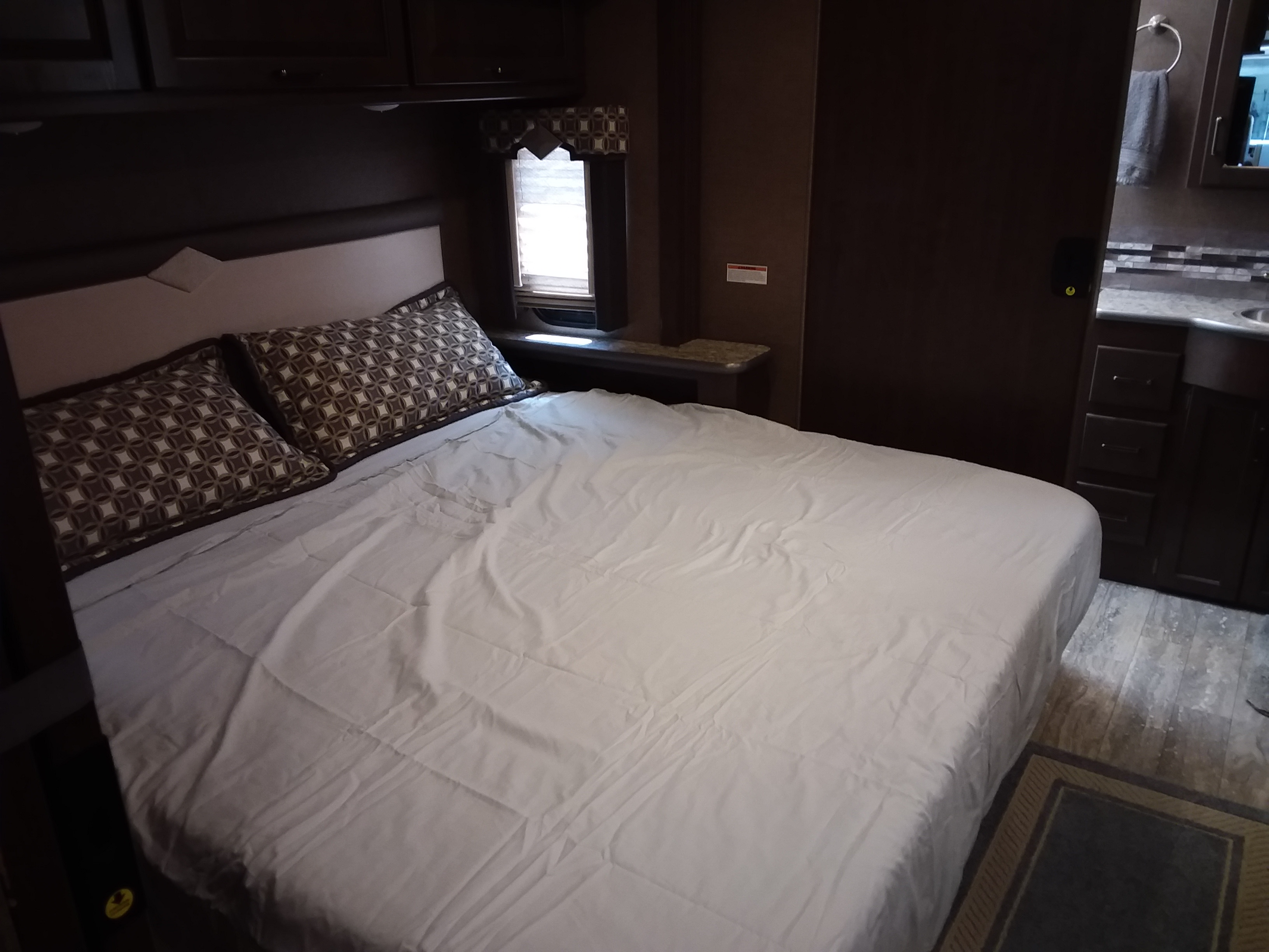 RV rental: comfortable bedroom with patterned pillows, crisp white bedding, and dark wood cabinetry.. Thor Hurricane 2019