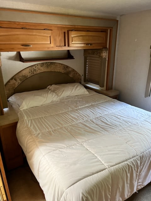 RV rental bedroom featuring a comfy bed with white bedding, overhead storage, and window, perfect for your travels.. Tioga SL 2006