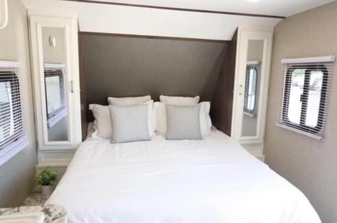 An inviting RV rental bedroom with a large bed, crisp white bedding, mirrored cabinets, and windows on either side.. Keystone RV Passport Ultra Lite 2019