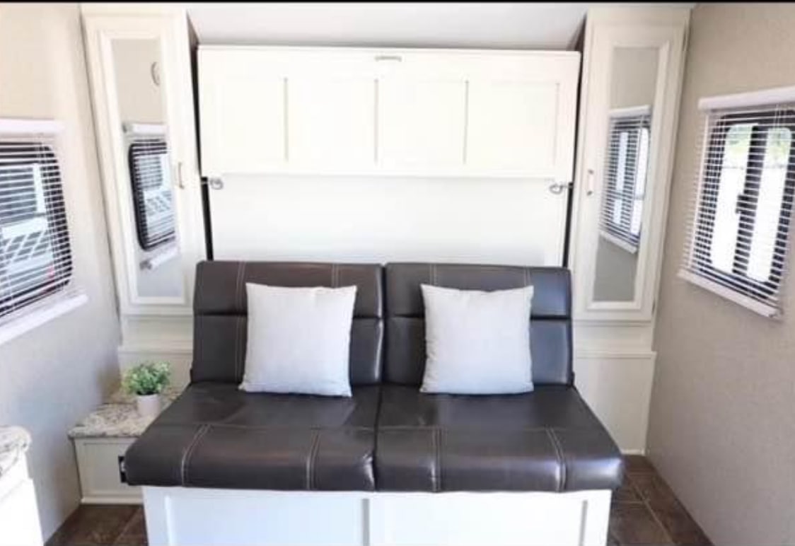 RV rental interior: a dark sofa with white pillows, a white wall-mounted bed, and side storage cabinets.. Keystone RV Passport Ultra Lite 2019