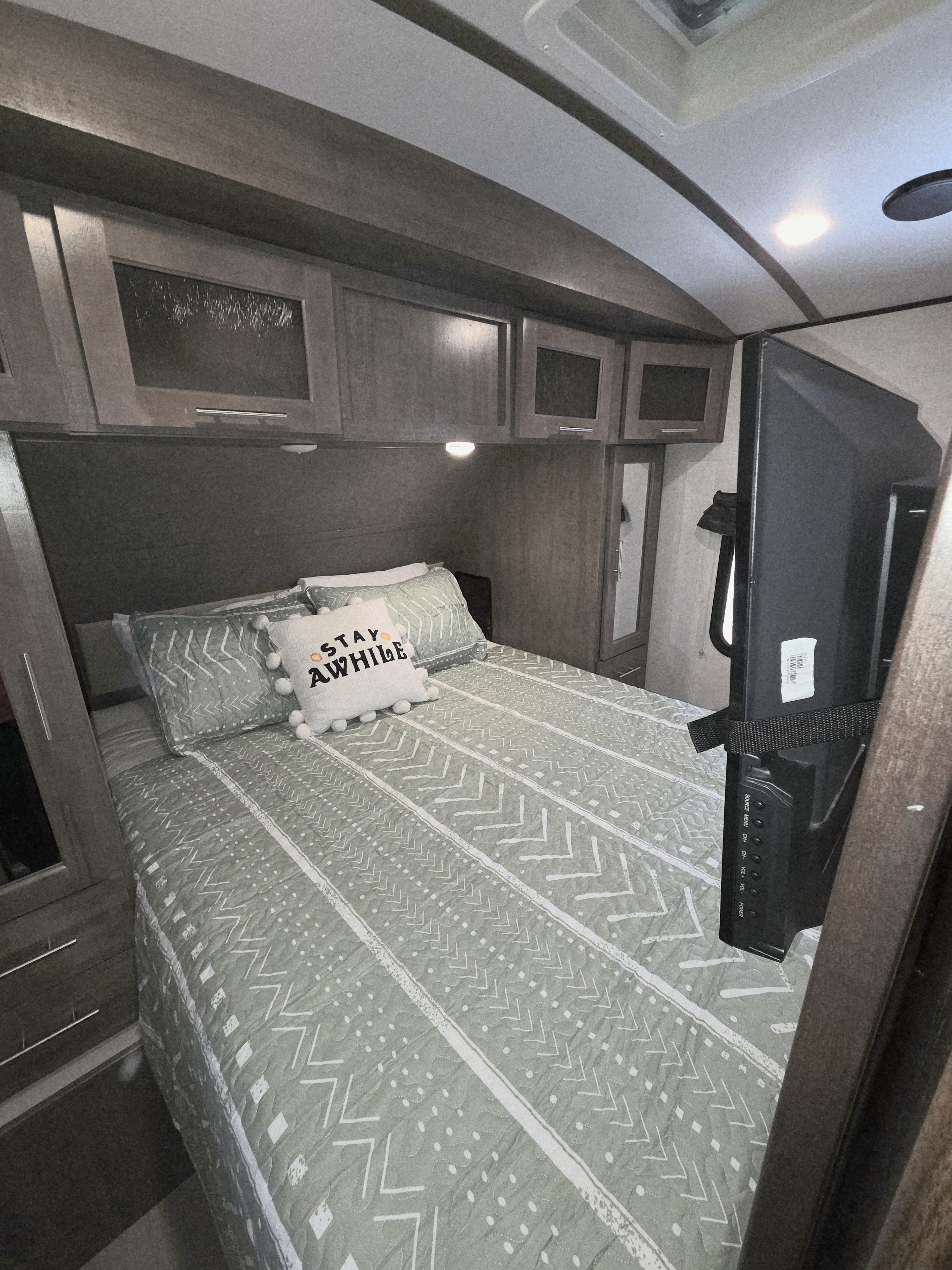 Cozy RV rental bedroom with patterned bedding, overhead cabinets, and a TV for comfortable travel.. Forest River Surveyor 2018