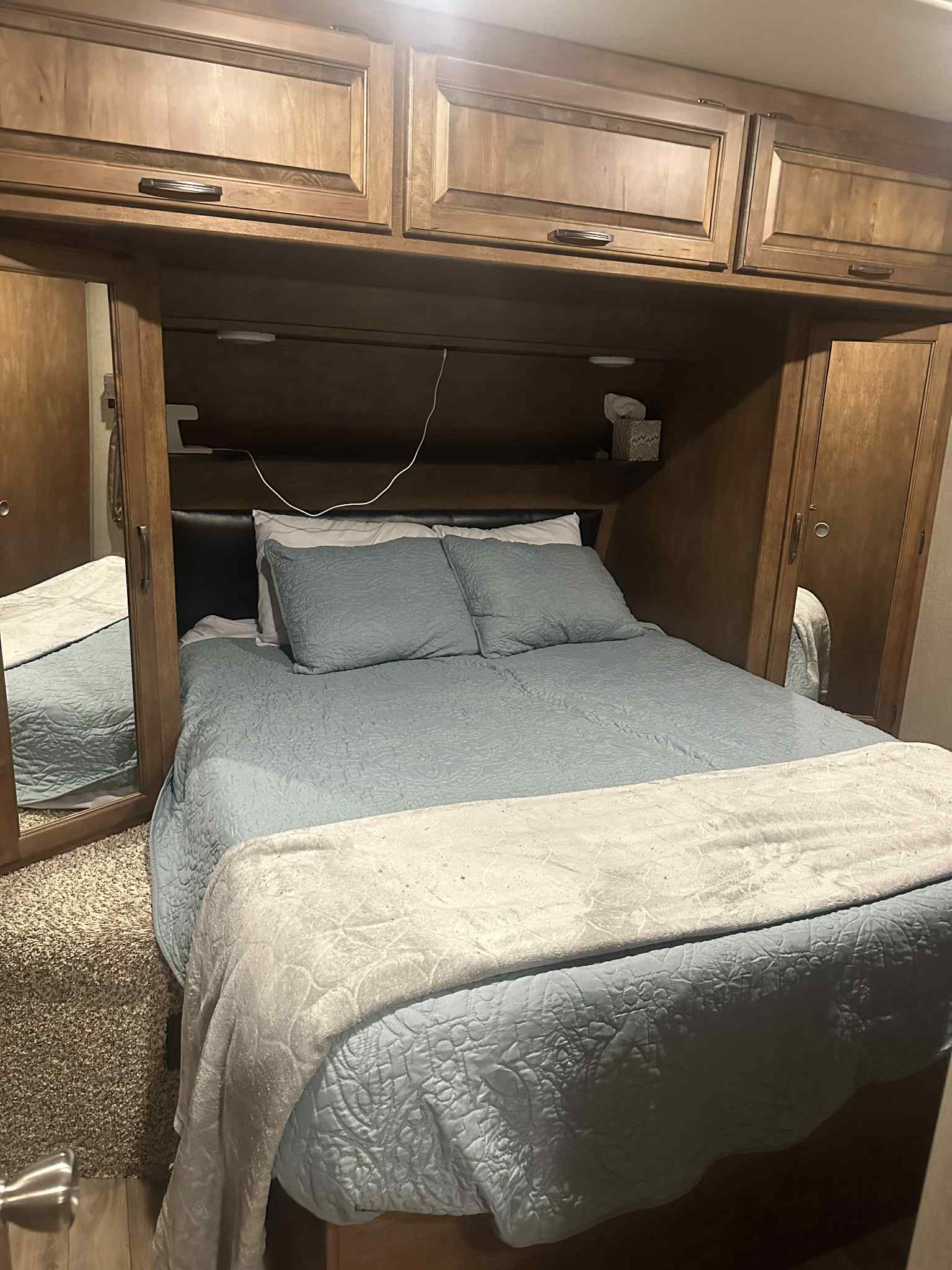 Inside a compact RV rental bedroom with a comfy bed, overhead cabinets, and a mirrored wardrobe.. Grand Design Reflection 2017
