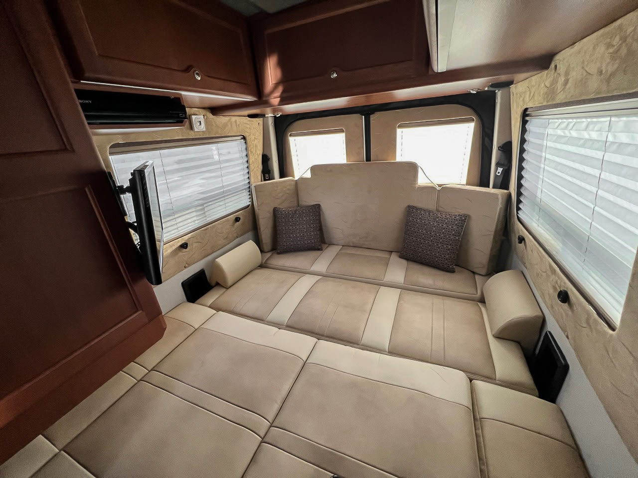 Spacious RV rental interior with a beige bed/lounge area, windows with blinds, and a mounted TV.. Roadtrek Roadtrek Class B 2015