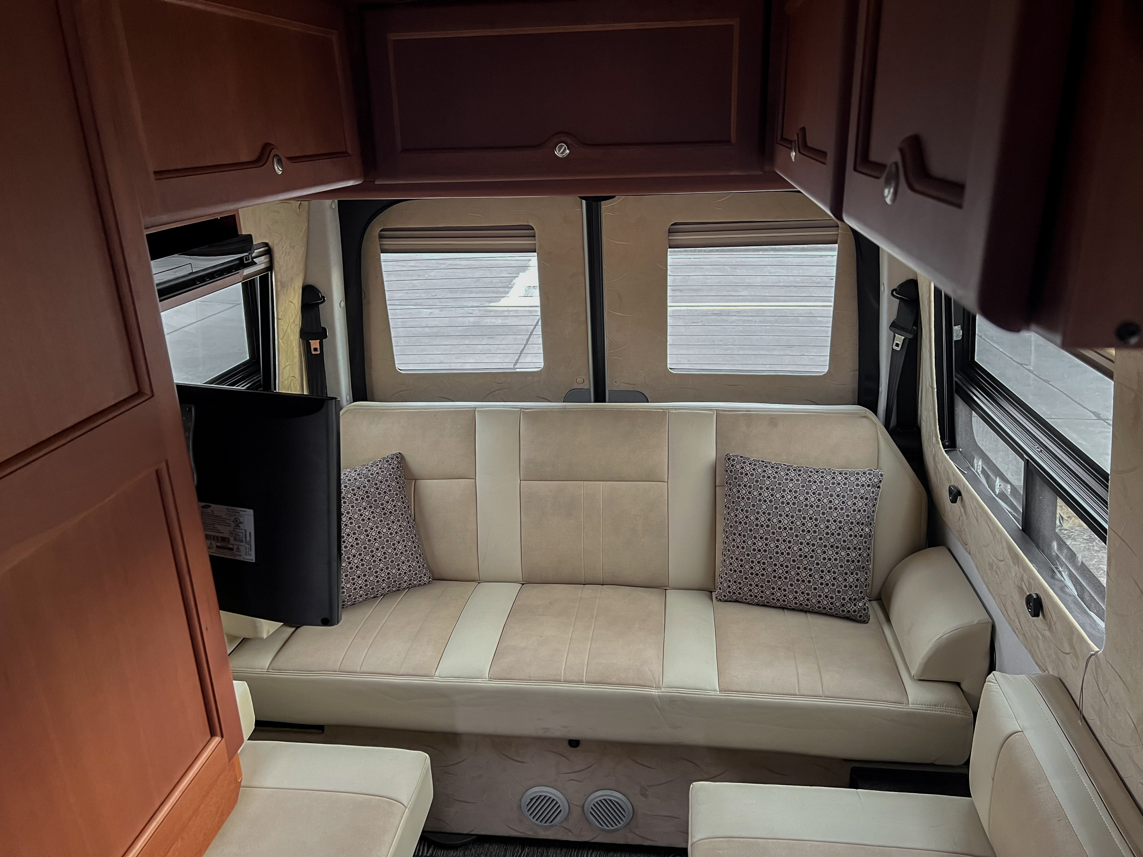 This cozy RV rental interior features a beige sofa, overhead wooden cabinets, and a TV, perfect for relaxing.. Roadtrek Roadtrek Class B 2015