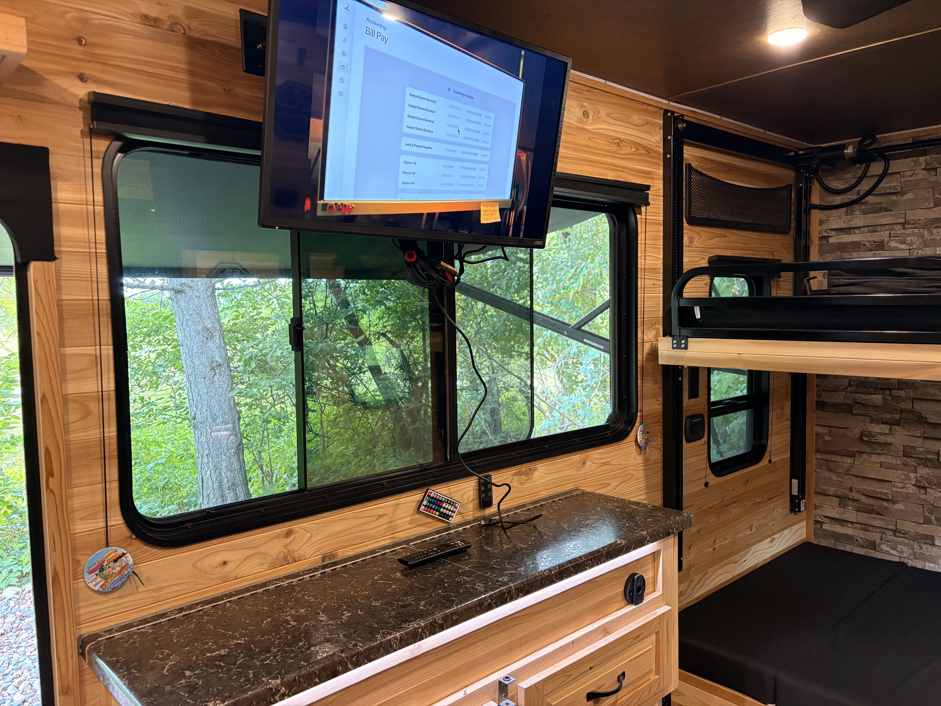 Inside an RV rental, a TV shows bill pay details above a counter. Wood paneling, large windows, and bunk beds fill the space.. Glacier RV Explorer 17 RV Explorer 2024
