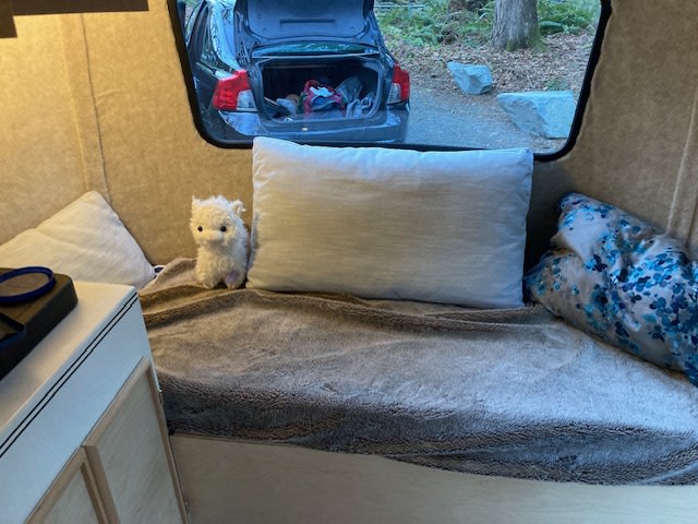 Inside a comfy RV rental: pillows, blanket, and a plush llama on a bench. Parked in nature, trunk open.. Scamp Scamp Trailer 1988