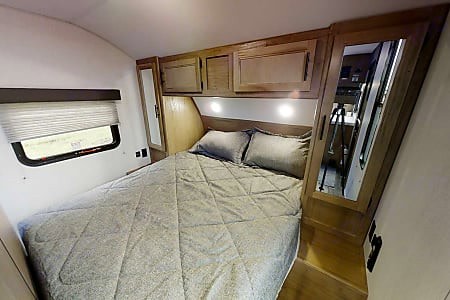 Cozy RV rental bedroom featuring a queen bed with gray bedding, overhead storage, and a large window.. Forest River Cherokee Grey Wolf 2023