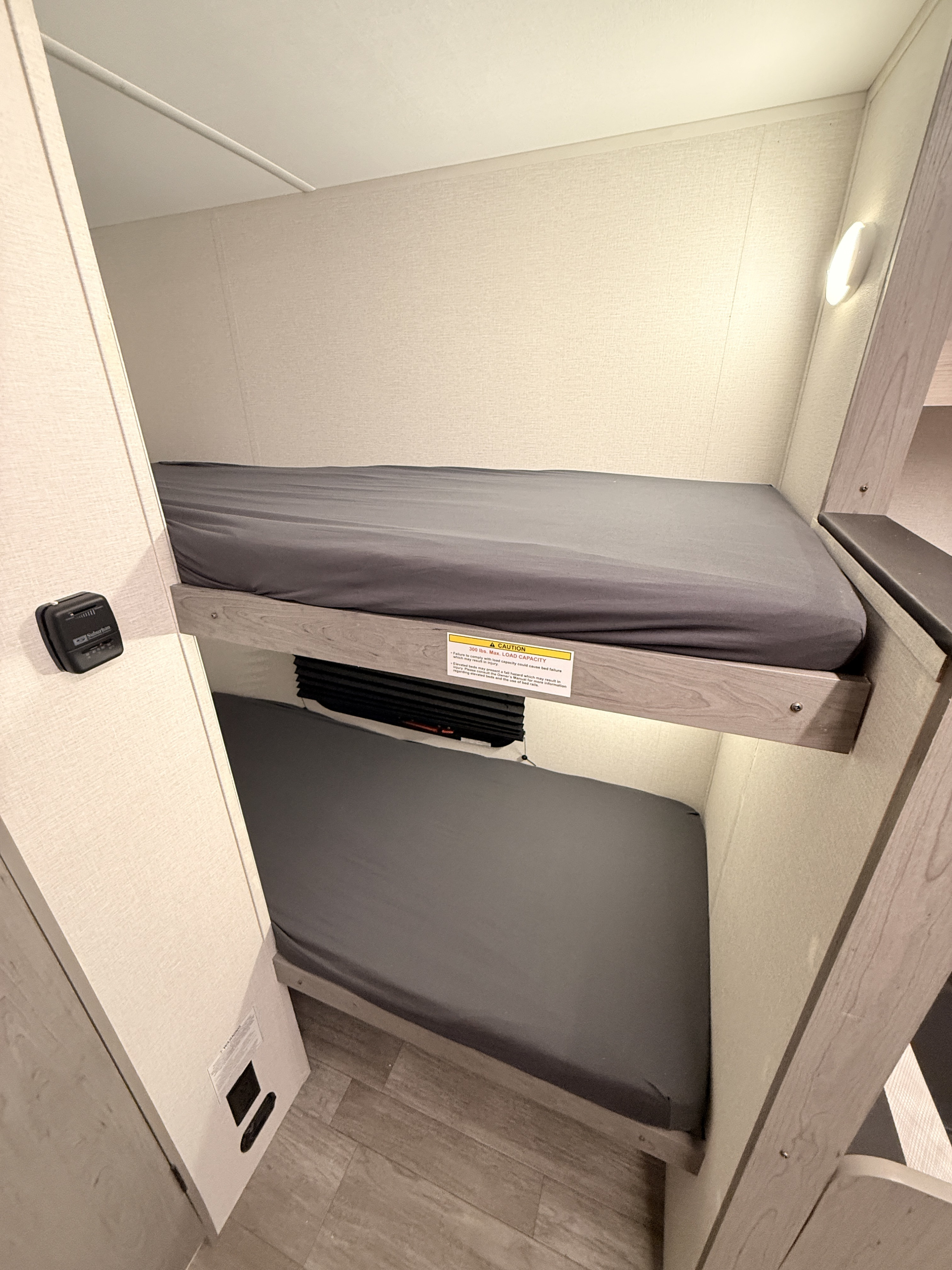 This RV rental interior showcases neat bunk beds with grey bedding, a wall-mounted thermostat, and accent lighting.. Heartland Mallard 2025