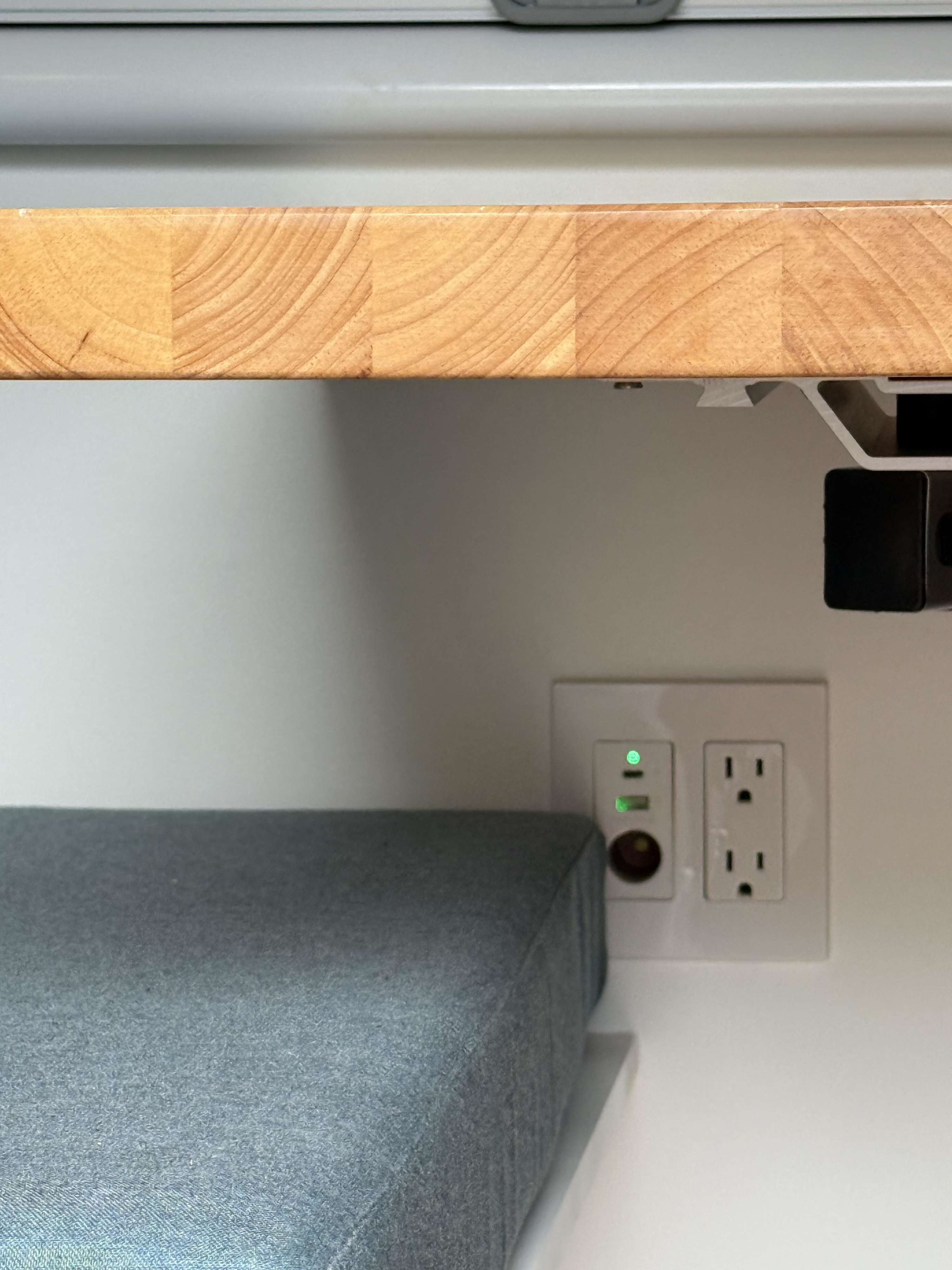 RV rental interior detail: wood counter, gray cushion, and white wall panel featuring USB, 12V, and standard AC power outlets.. Dodge Dodge 2023