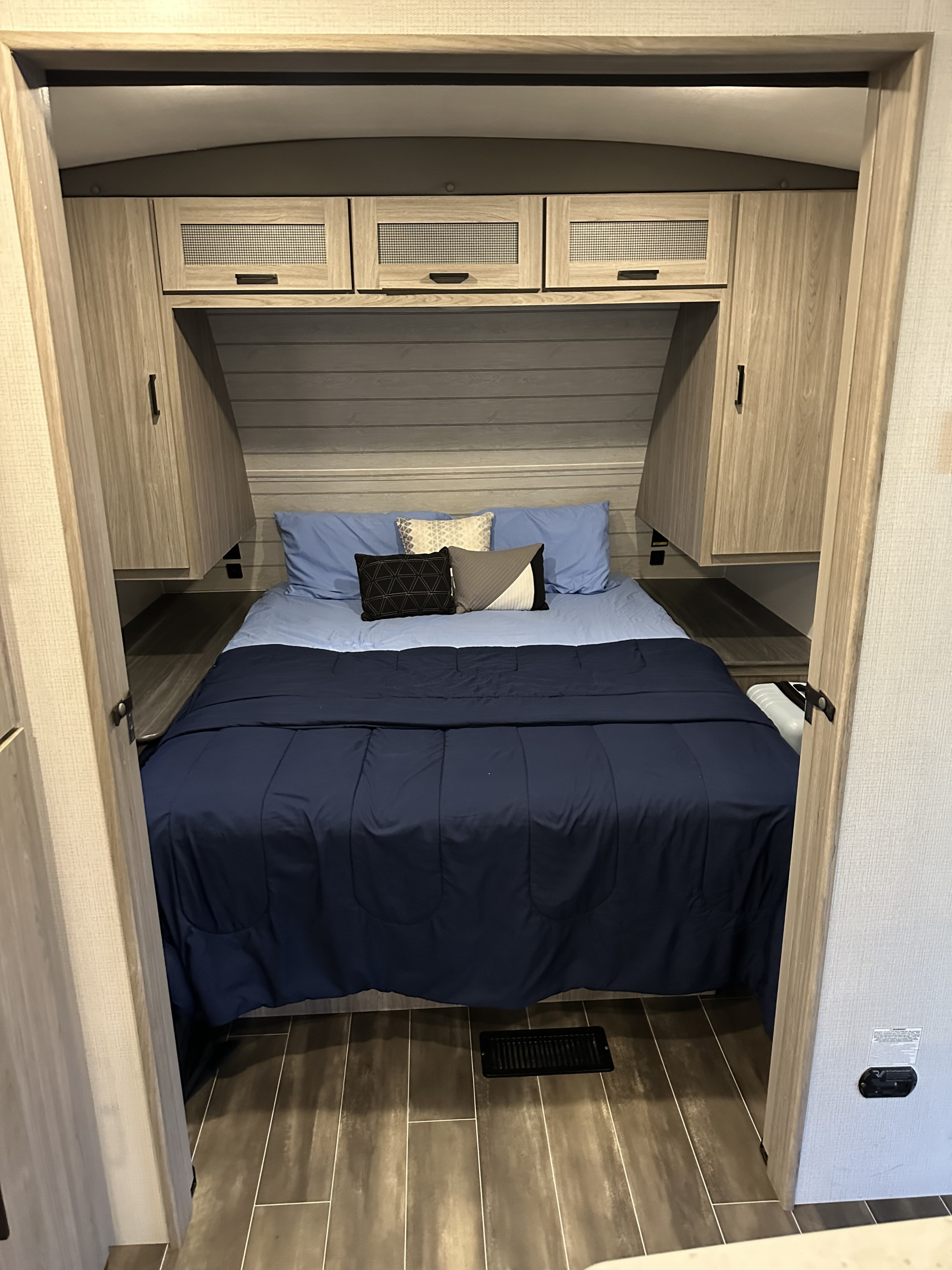 Inside an RV rental bedroom, showcasing a bed with blue linens, overhead storage, and side closets.. Keystone RV Passport GT Ultra Lite 2023